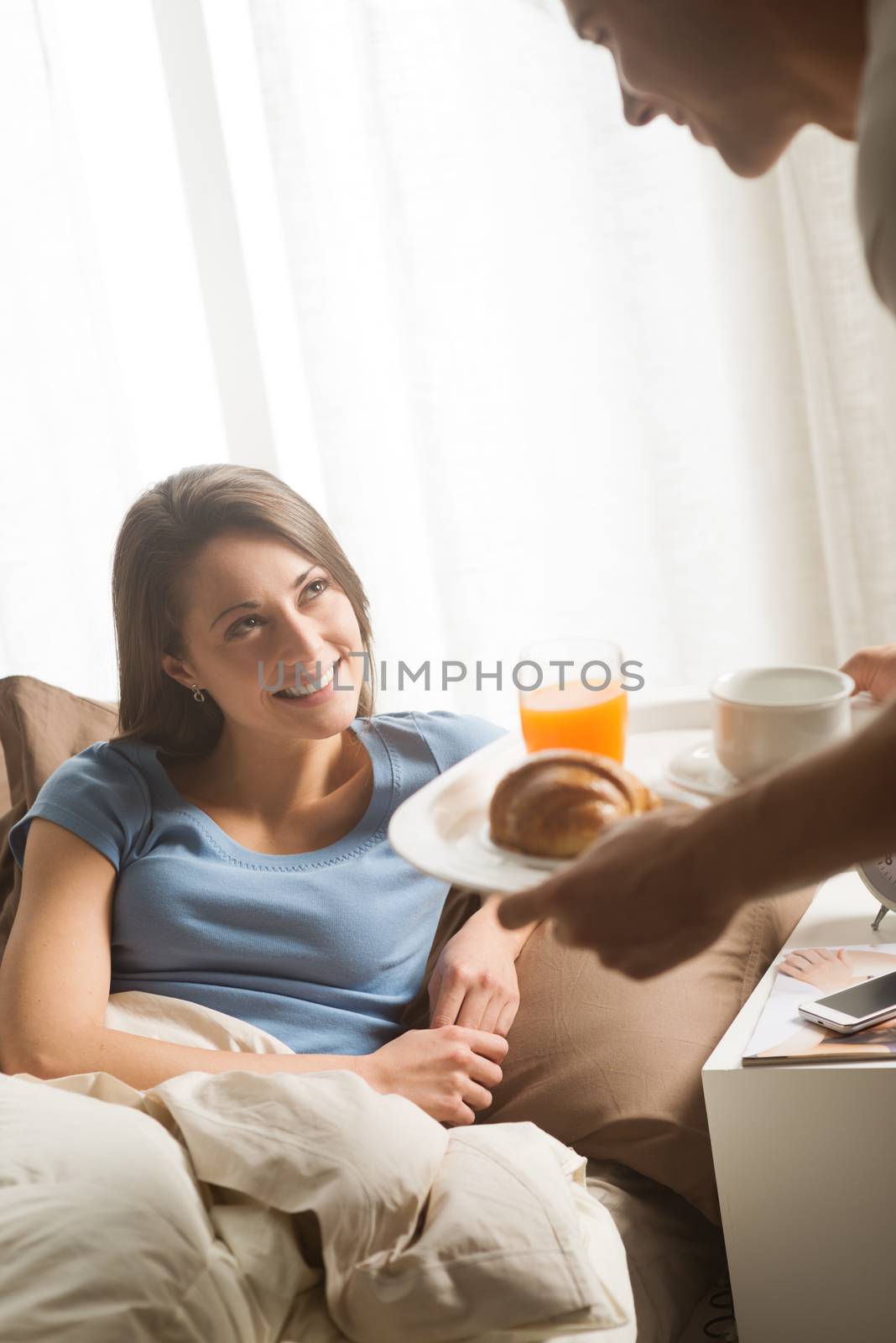 Hand holding breakfast tray to a happy relaxed woman in bed 