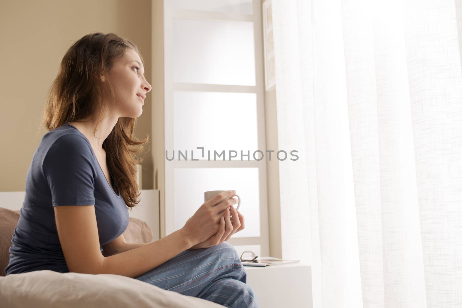 Portrait of a pretty young woman holding a cup of coffee in bed