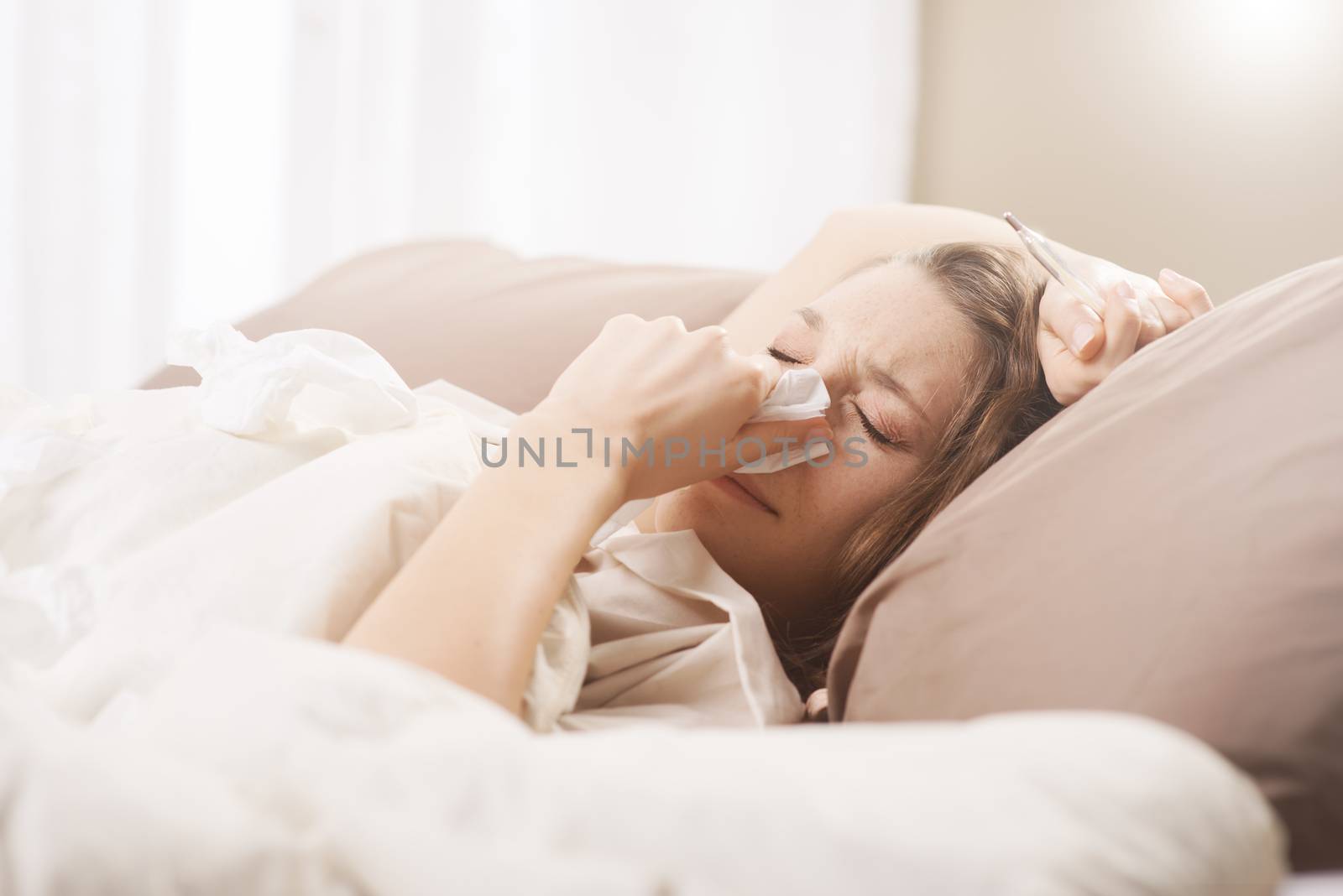 Young sick woman blowing her nose while in bed
