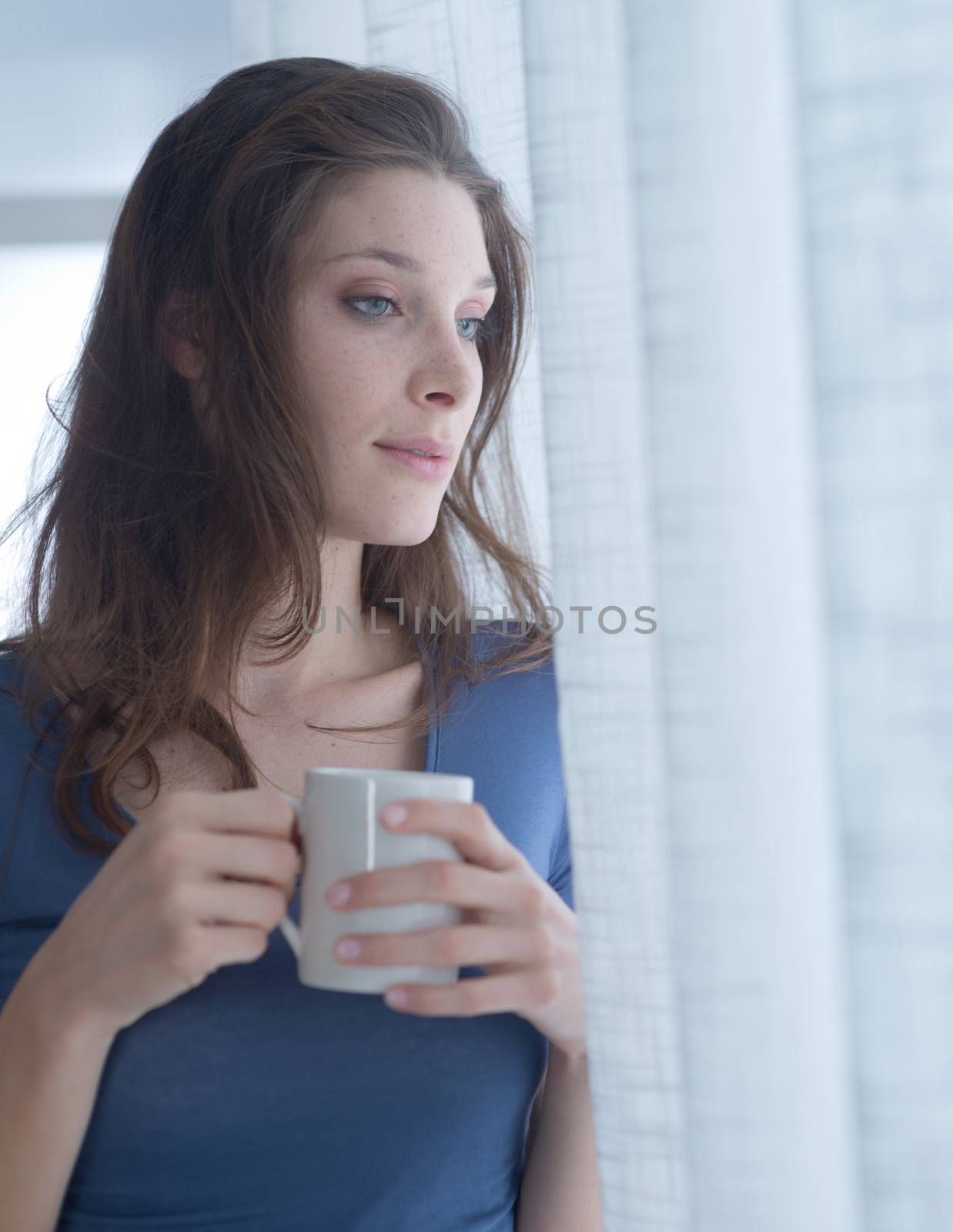 Beautiful woman with cup of coffee looking out of window. 