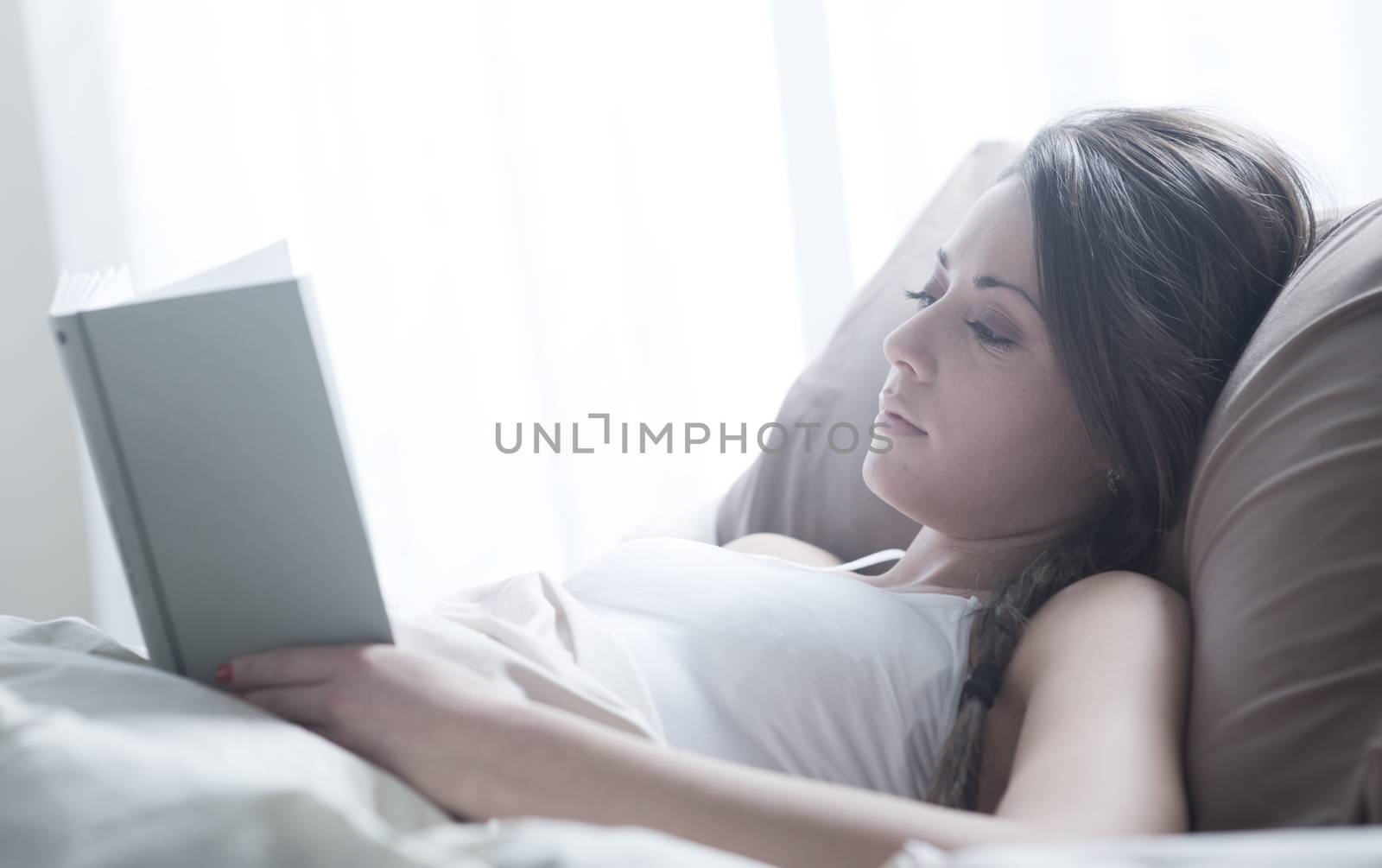 Woman lying in bed while reading a book 