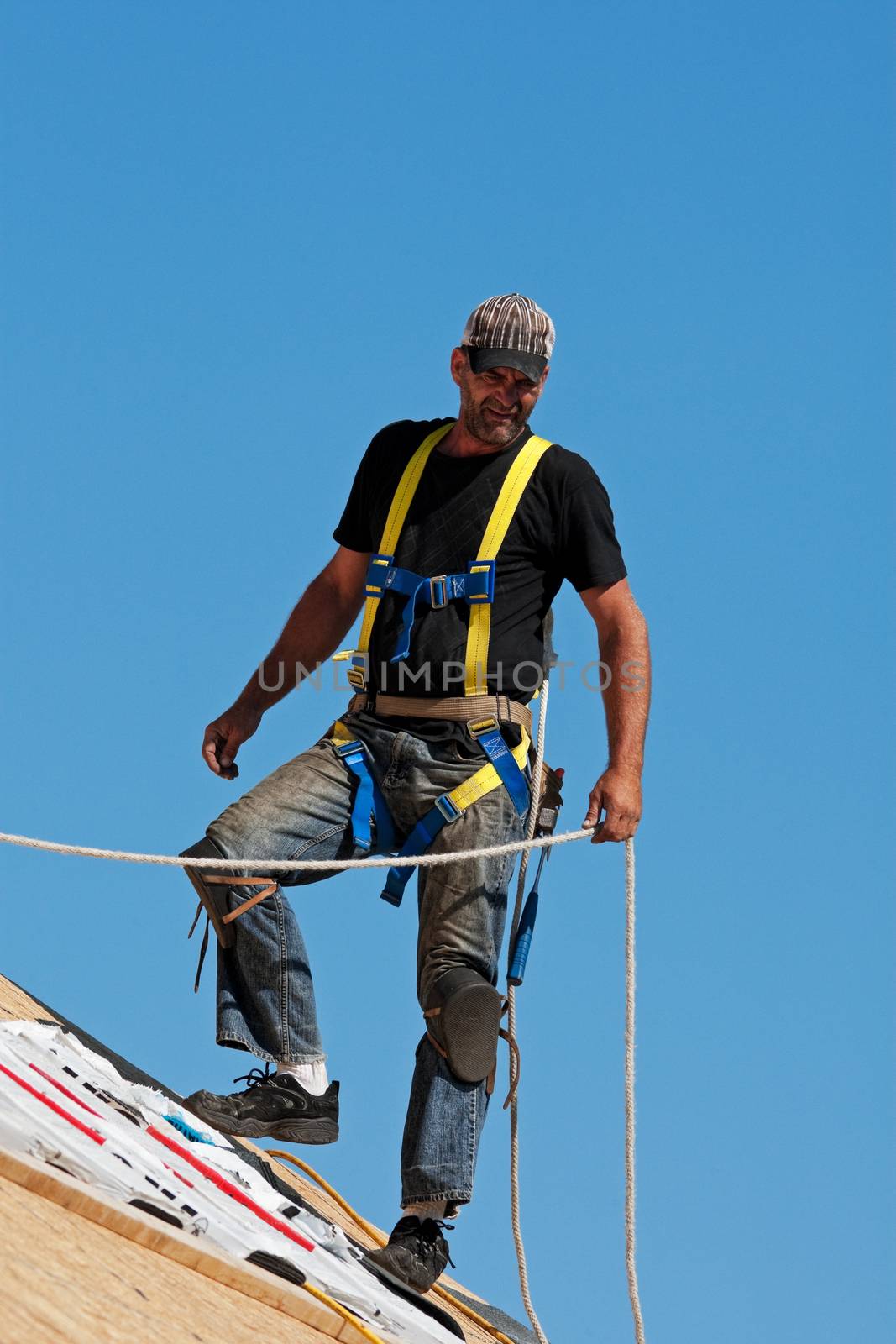 Roofer with safety harness shingling a roof with a steep pitch.