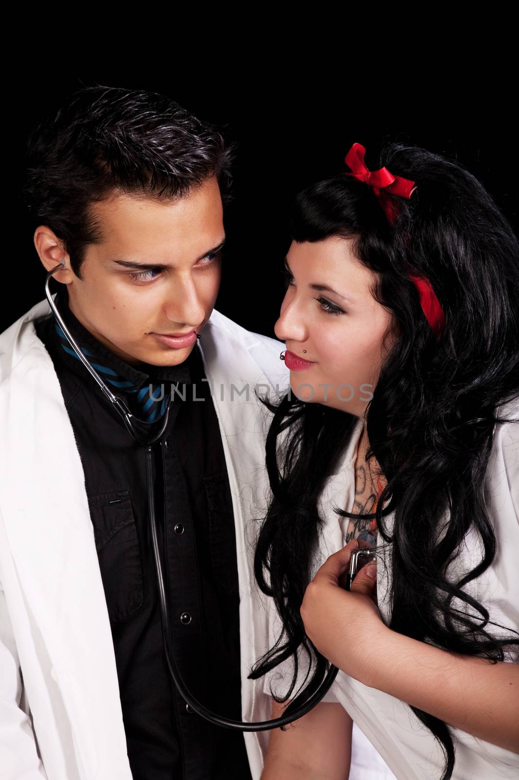  Two high school kids in a school play.  A nurse holds a stethoscope to her heart so the doctor can here her heartbeat for him. 