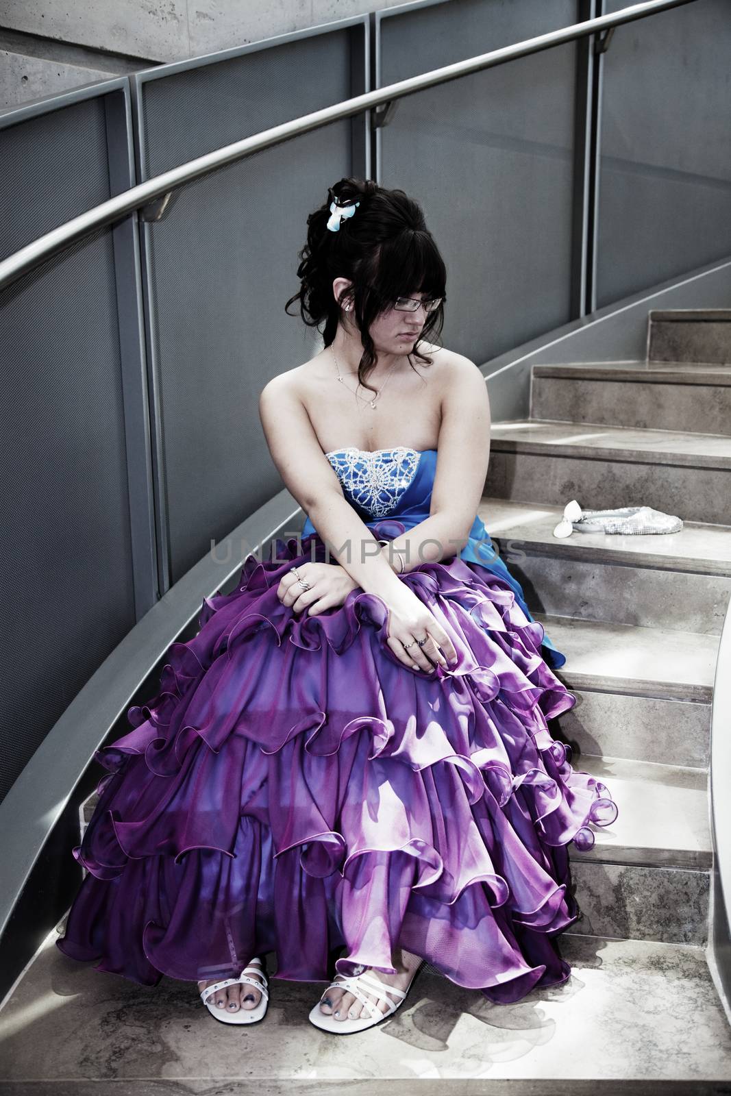 A young girl sits alone in her prom dress on a lonely flight of stairs.