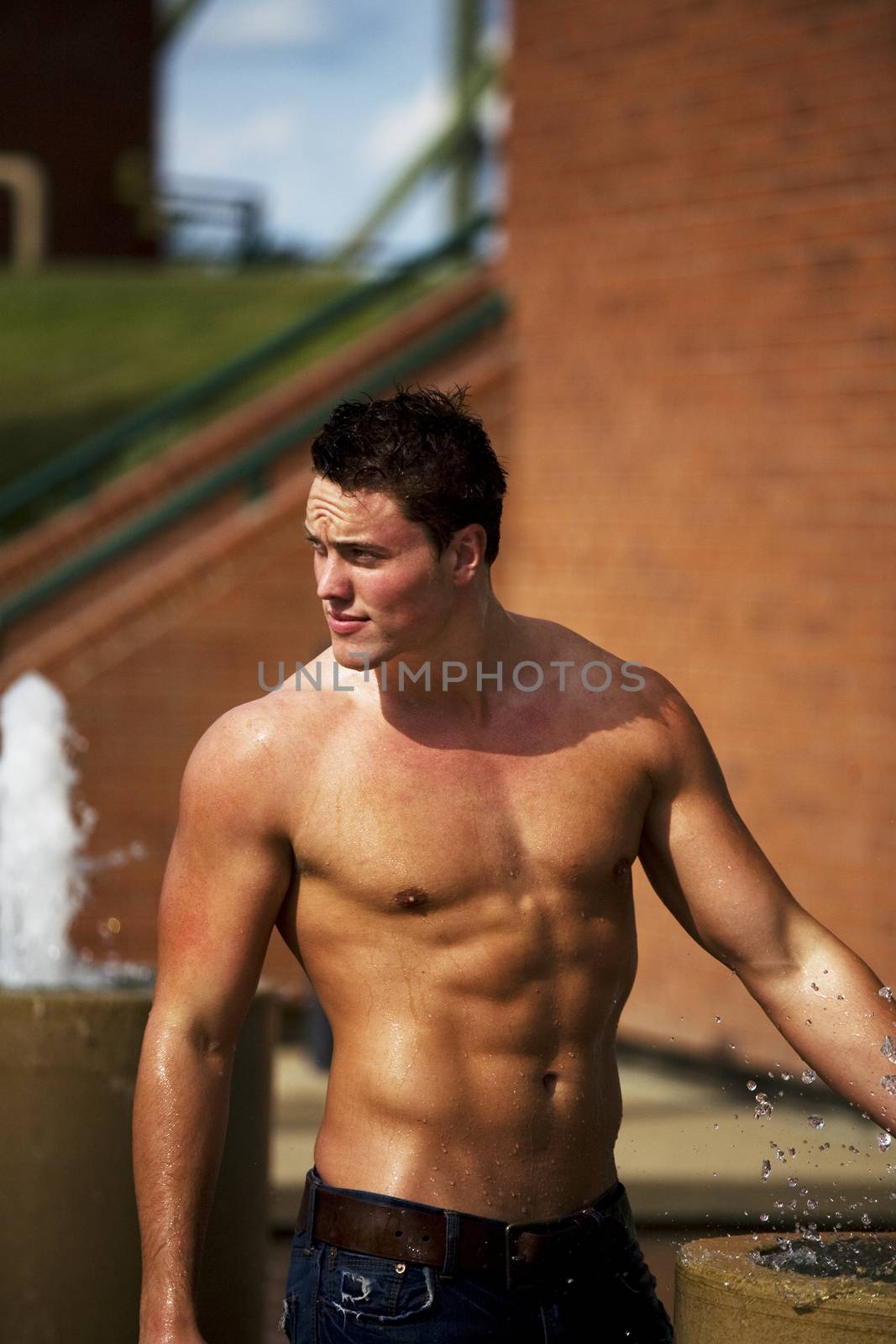A young bodybuilder cooling off in a fountain on a hot summer day.