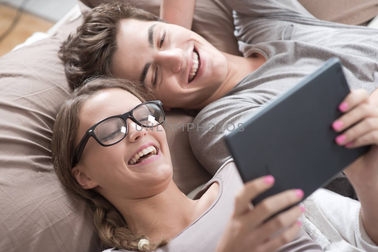 Two happy friends lying in bed using a digital tablet together 