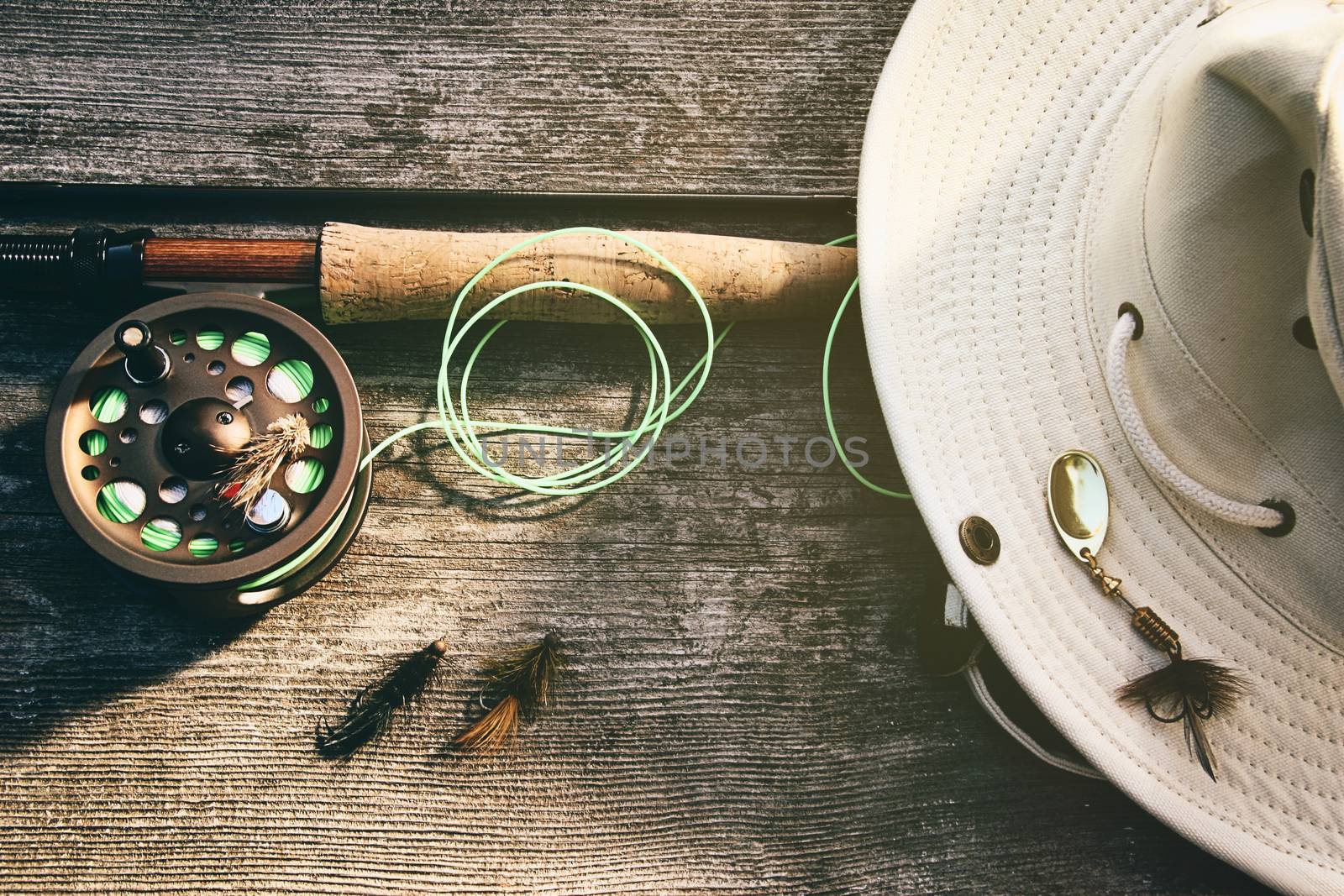 Fly fishing rod with hat on wood by Sandralise