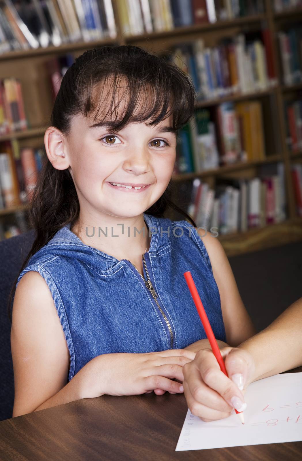 A child smiling from her desk in the school library.