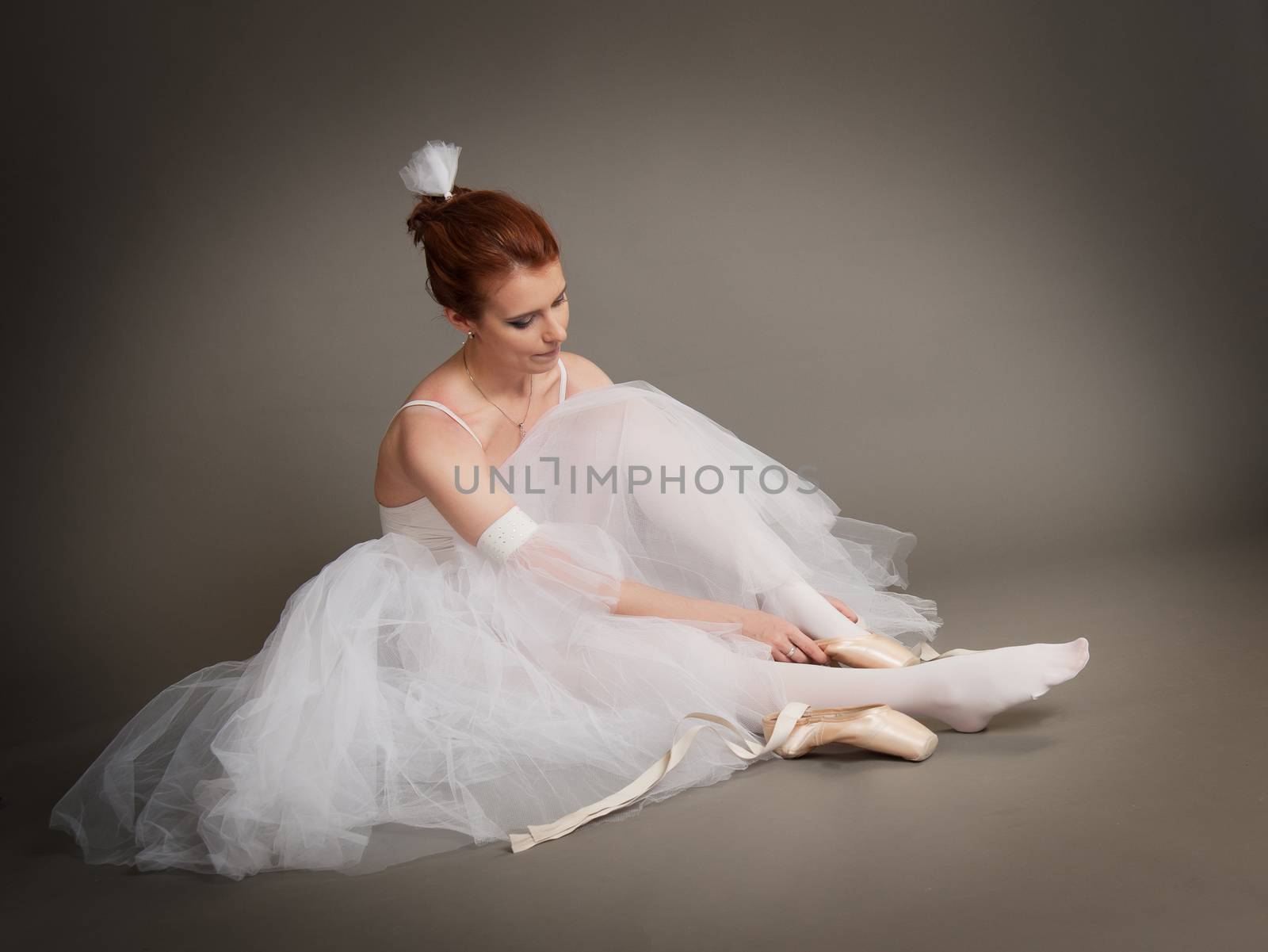 dancer wears pointes,sitting on the floor on a grey background