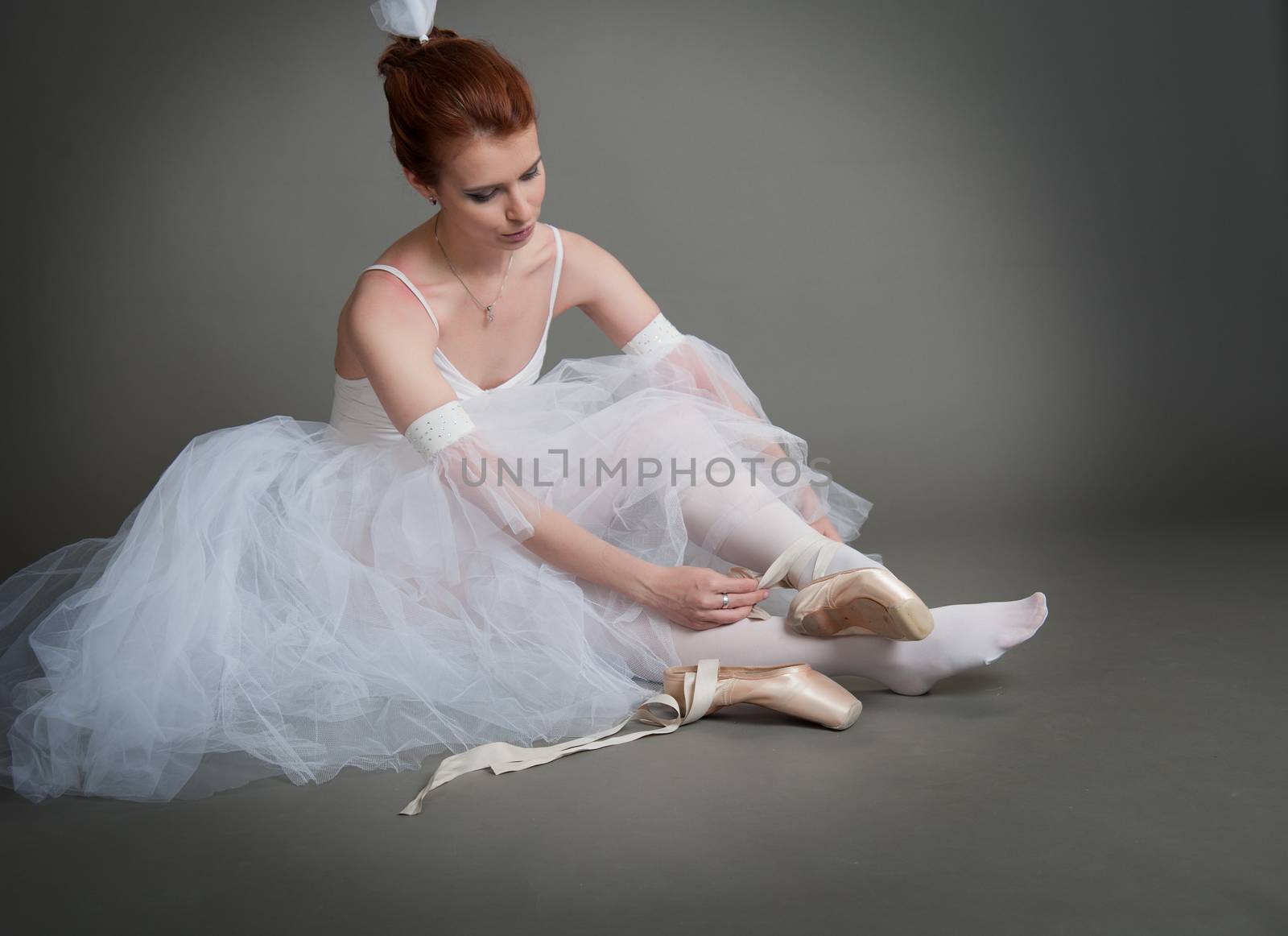 dancer wears pointes,sitting on the floor on a grey background