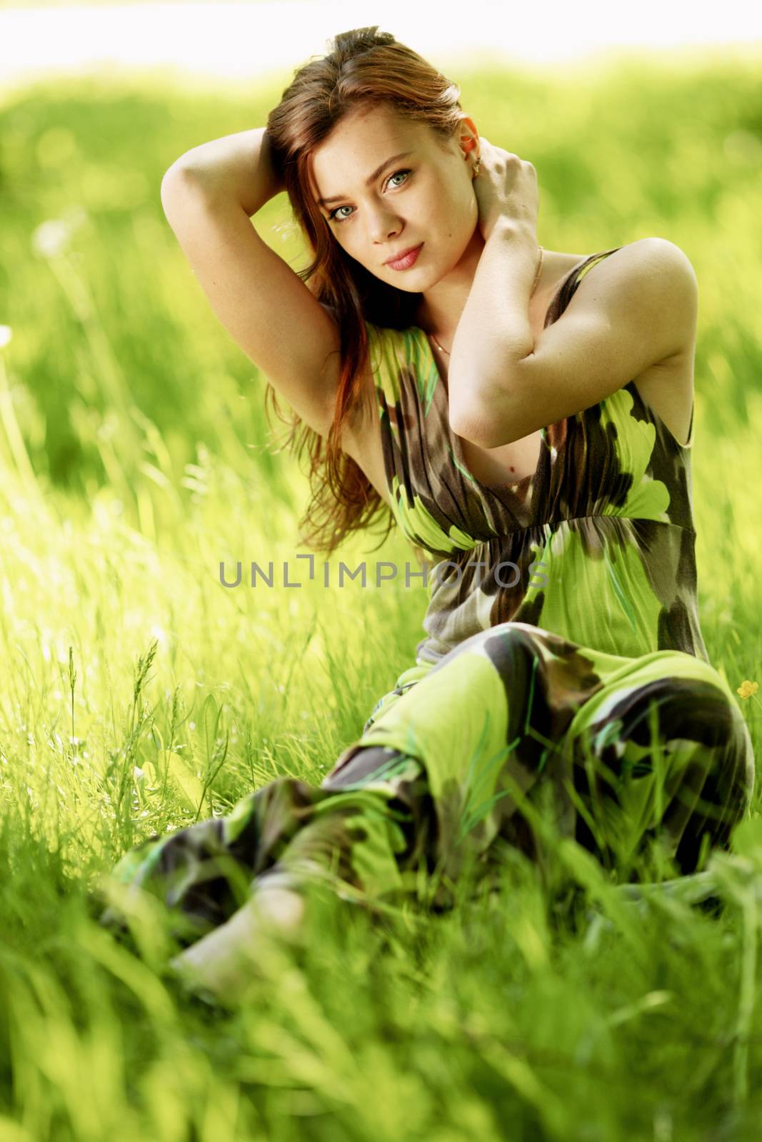 Beautiful woman sitting in a green field enjoying the summer sunlight