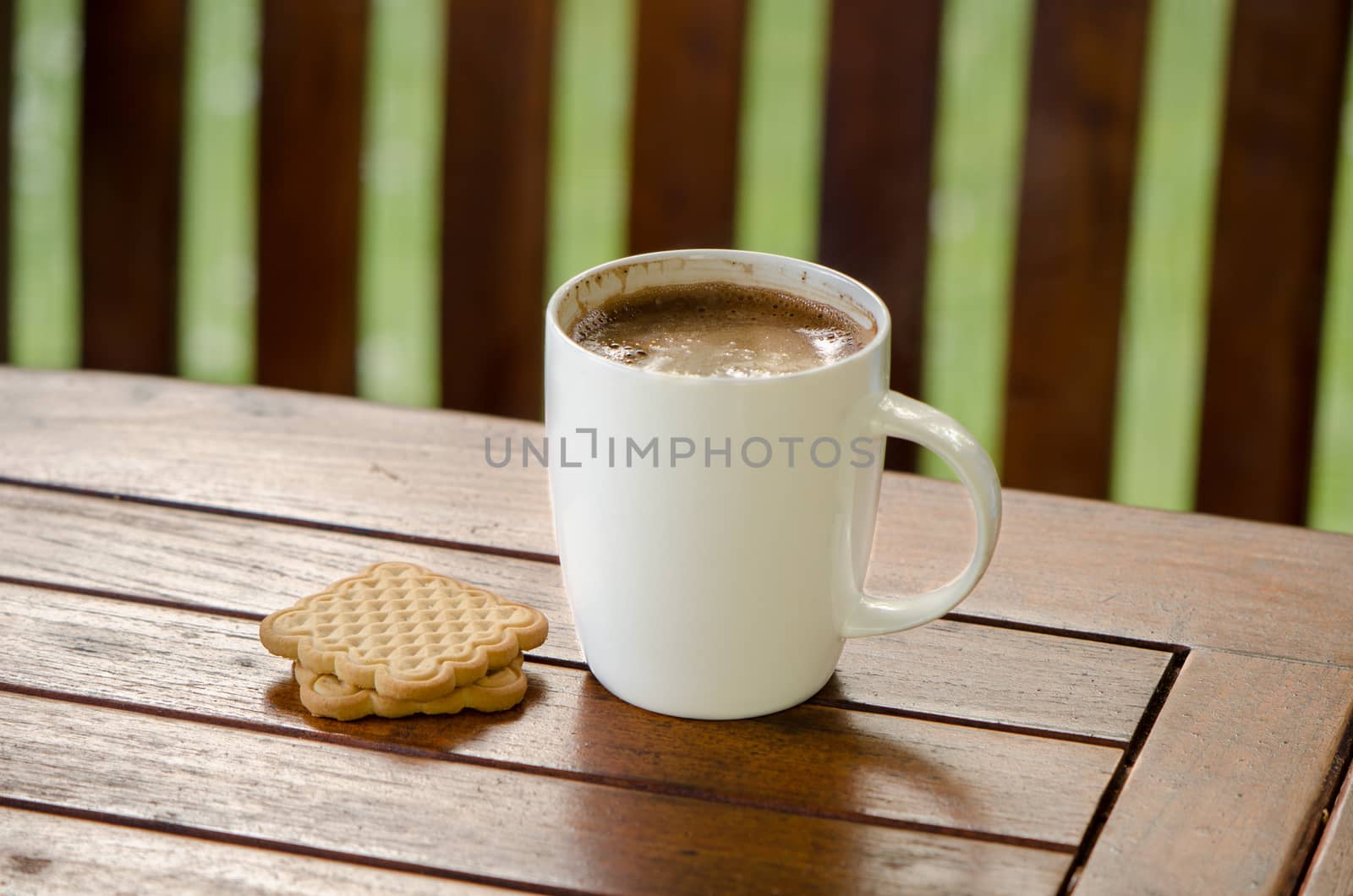 Cup of steaming hot coffee in white cup and cookie biscuit on table in outdoor bower.