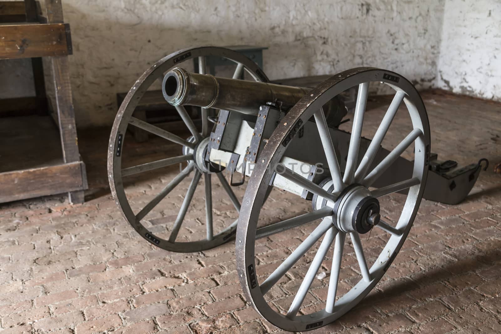 Antique civil war cannon with giant wheels displayed in an old room.