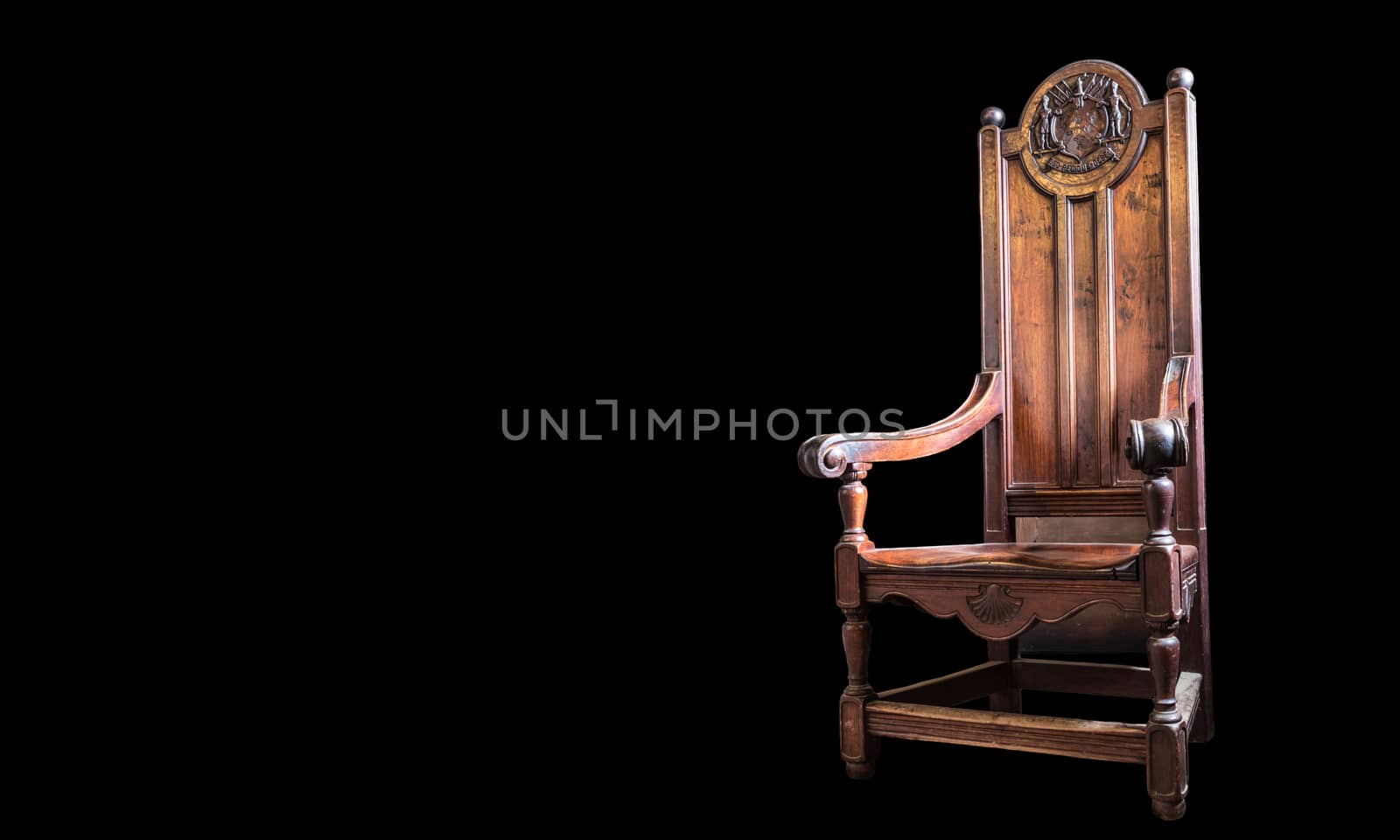 Heavy wooden high backed chair with beautiful scrollwork and craftsmanship. On black background.