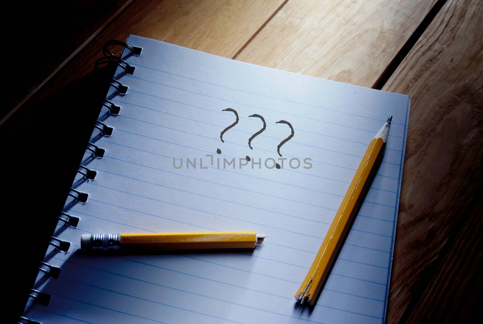 Three questions mark and broken pencil on top of a note pad 