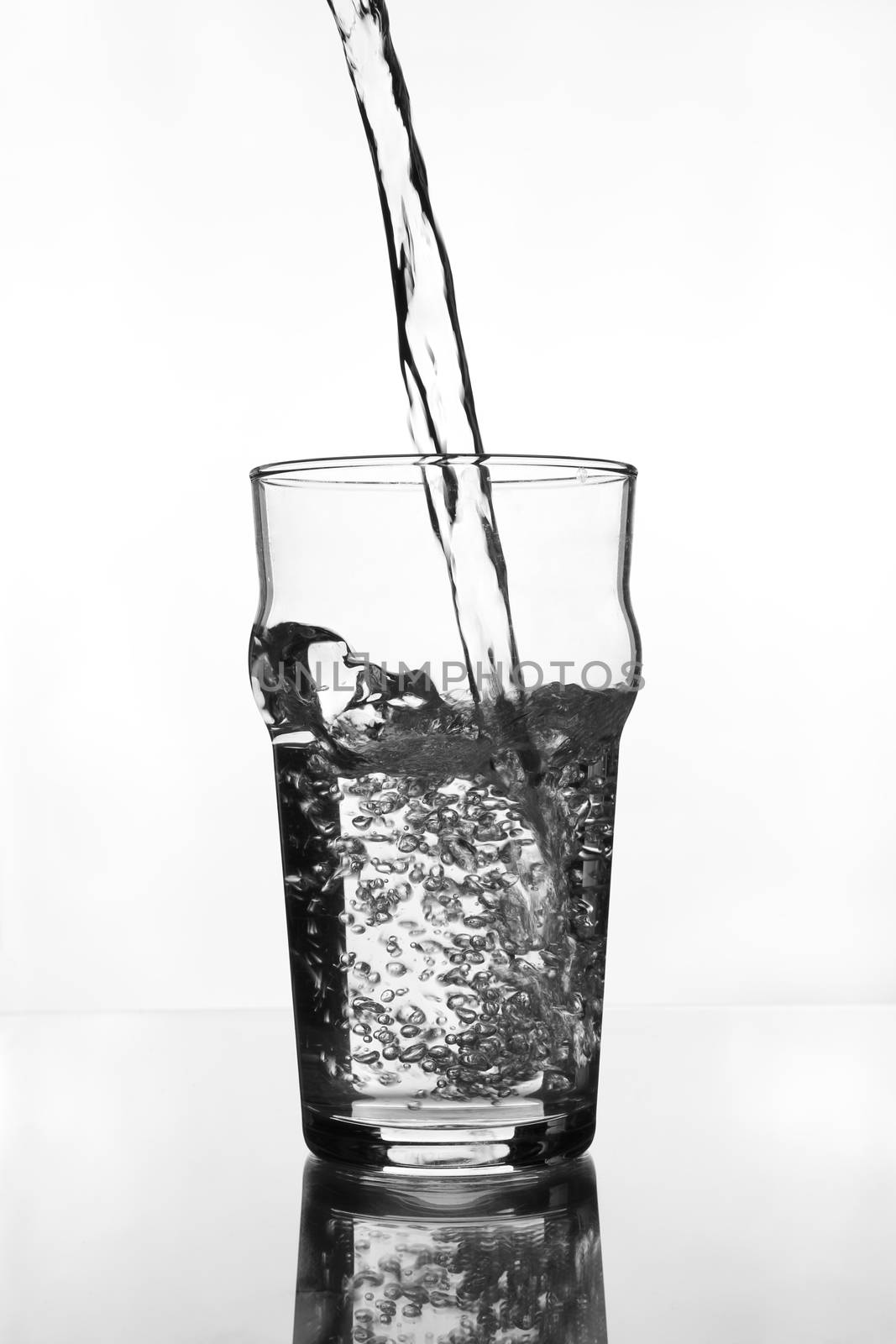 wine glass with water pouring on glass table (gray scale)