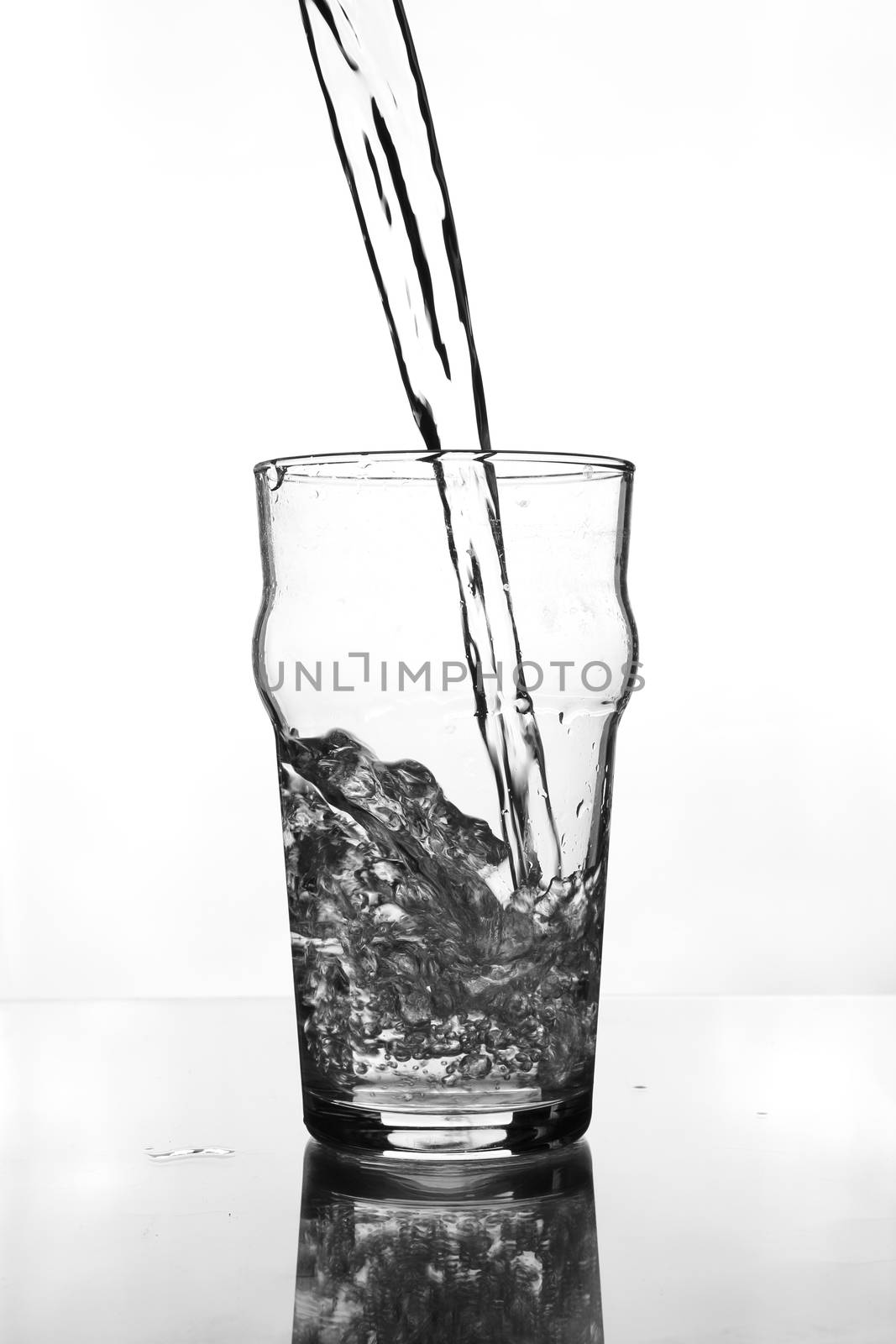 wine glass with water pouring on glass table (gray scale)