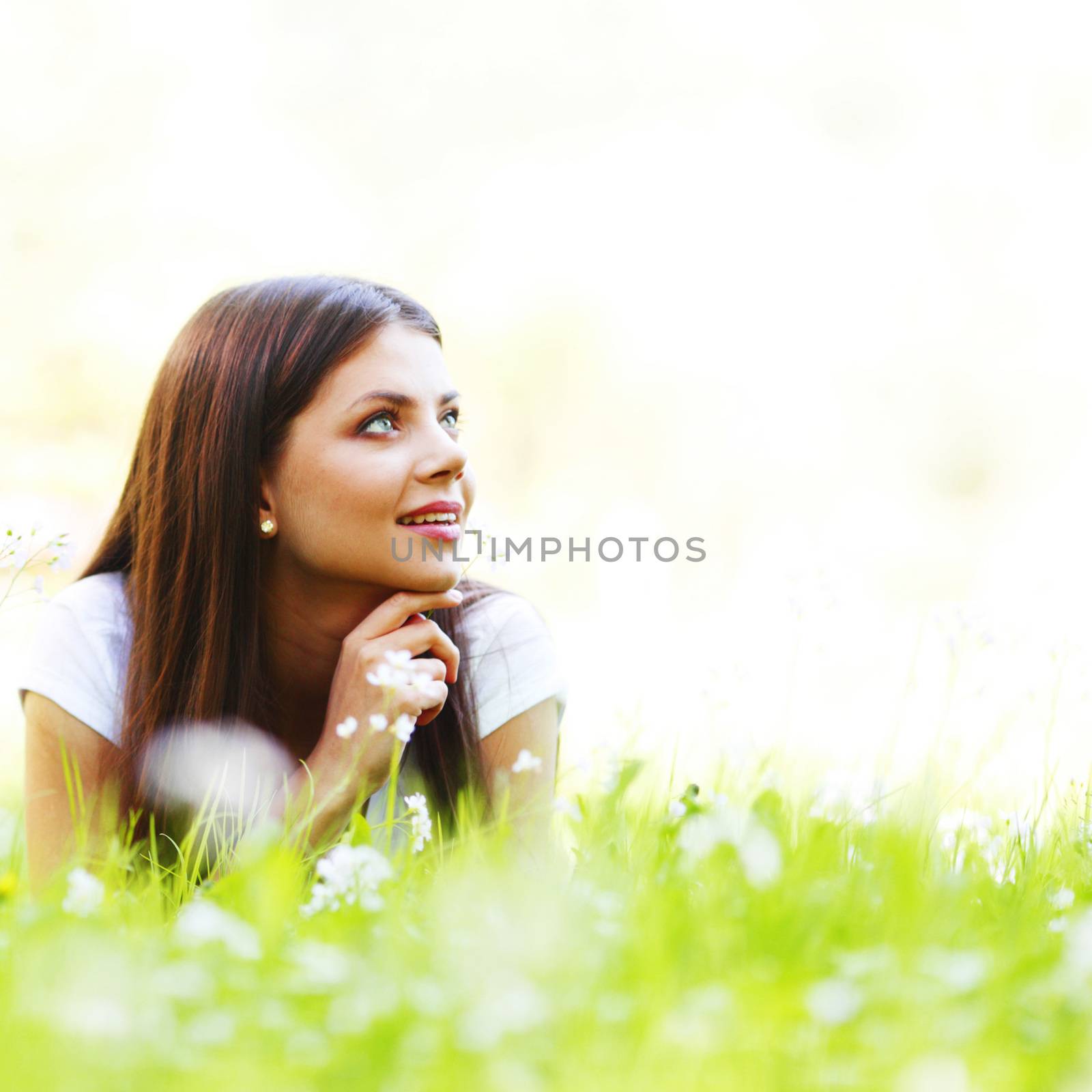 Pretty brunette girl laying on grass with white  flowers around her