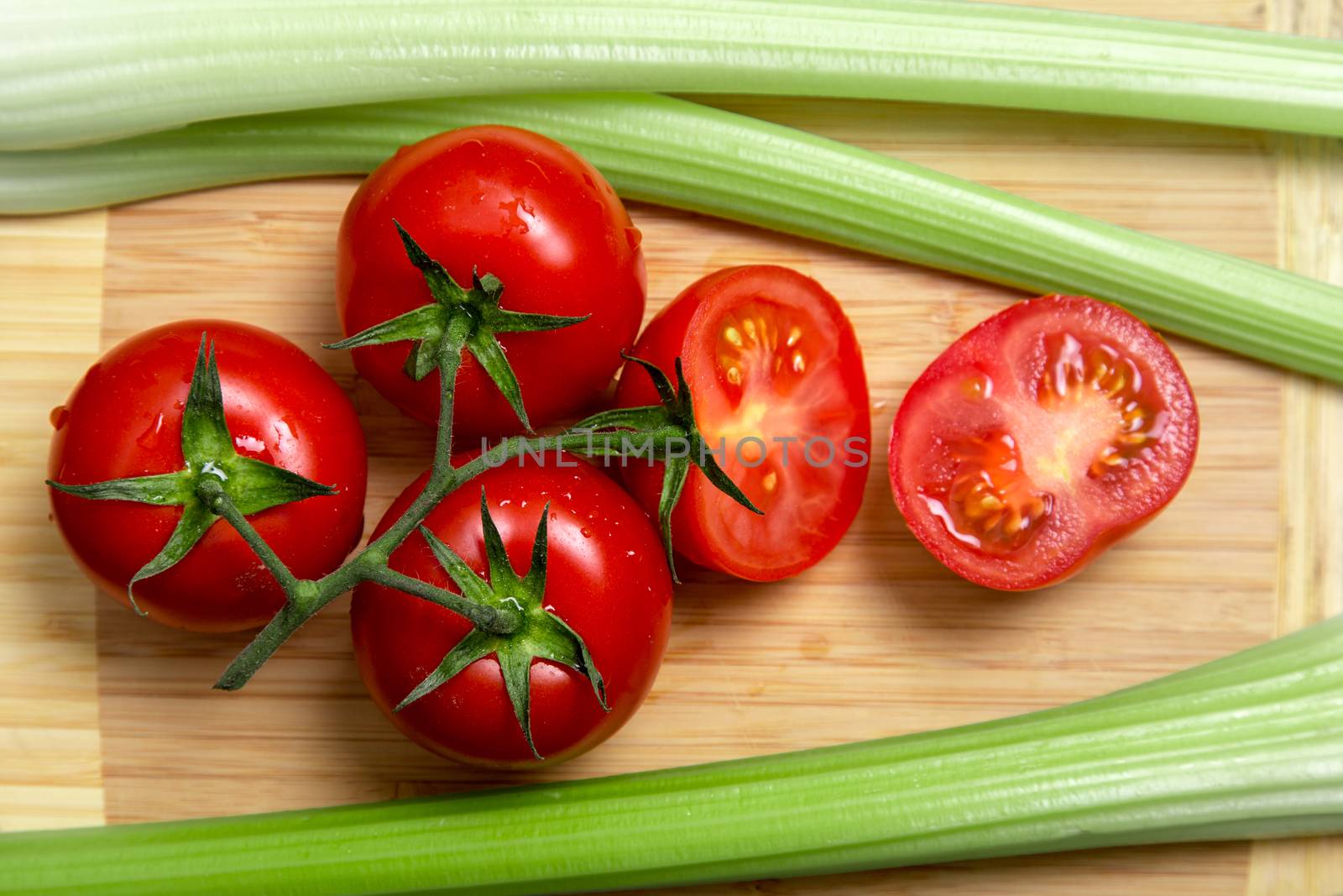 High angle view of bunch of fresh tomatoes and celery sticks on wooden chopping board 