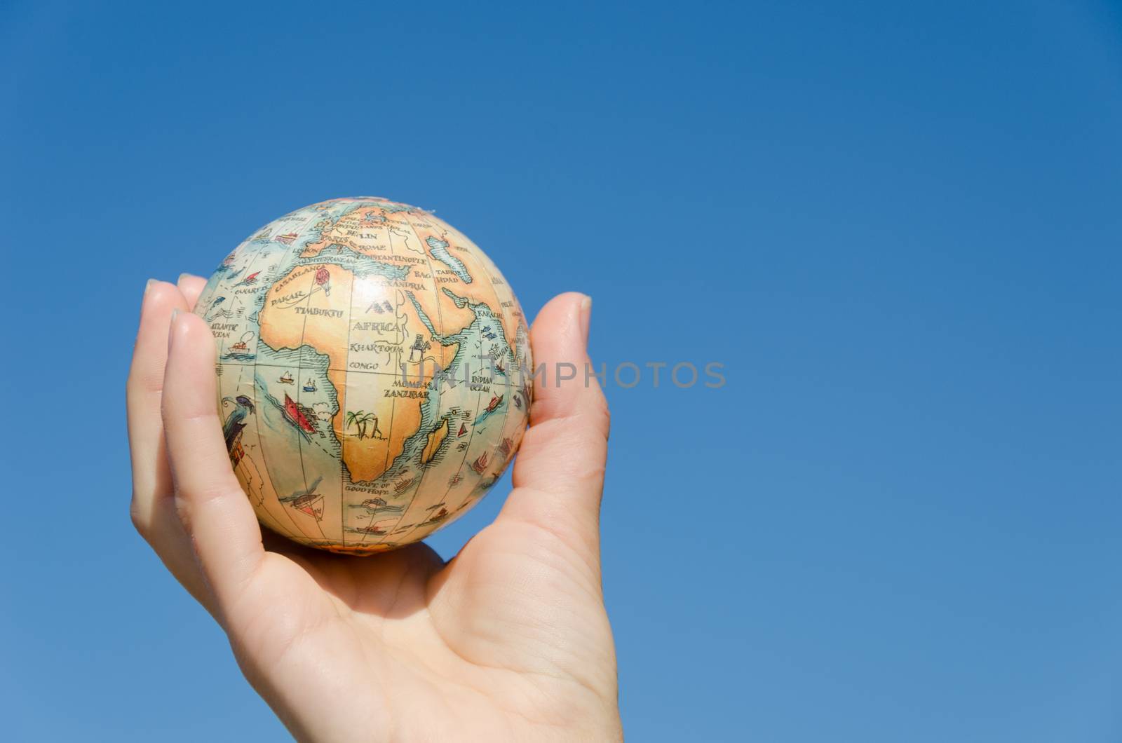 earth globe miniature model in female palm on blue sky background, Africa, symbolizing environmental care.