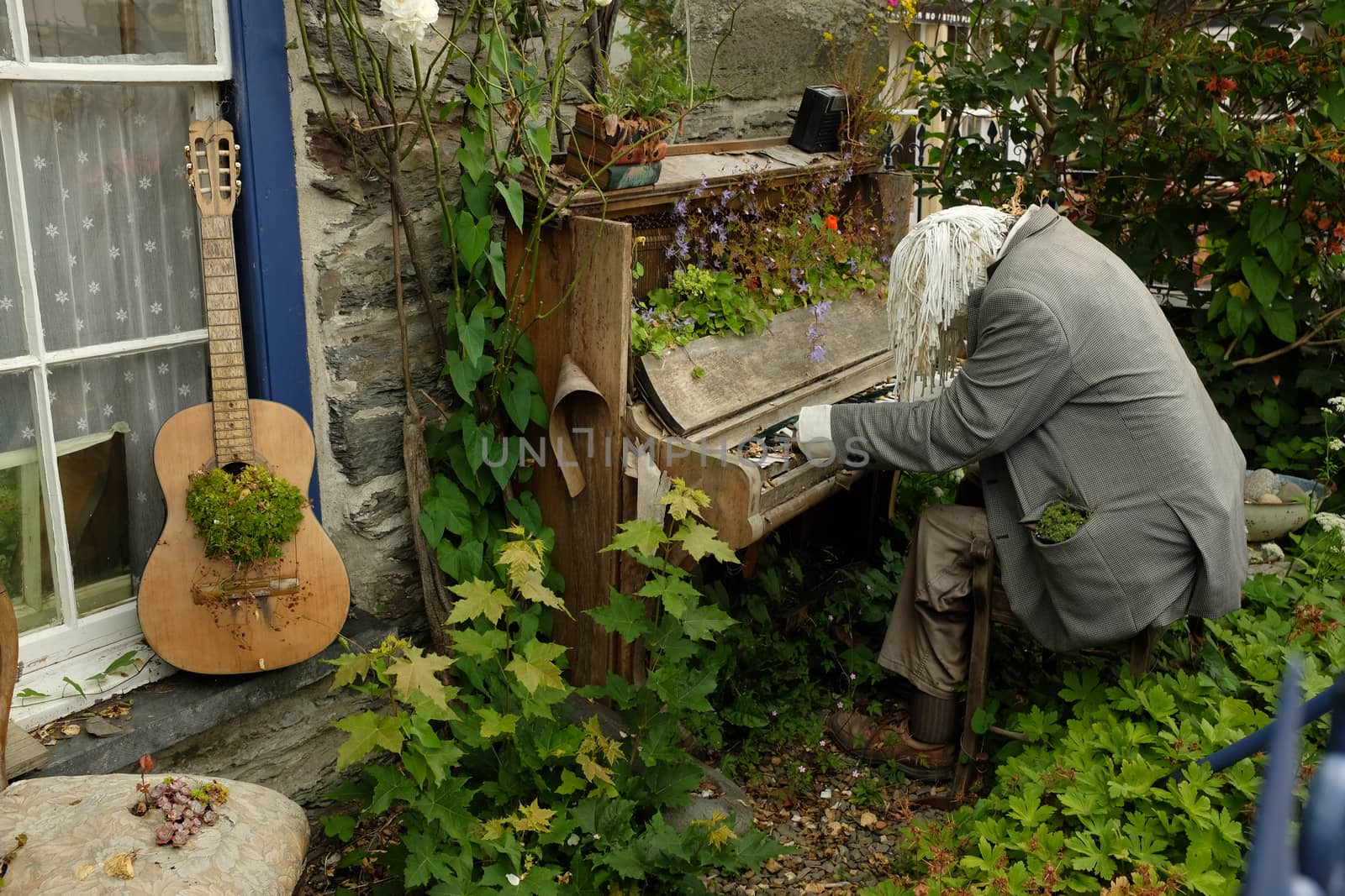 An overgrown garden with a dummy placed as a pianist with an old brocken piano and a guitar with plant growing.