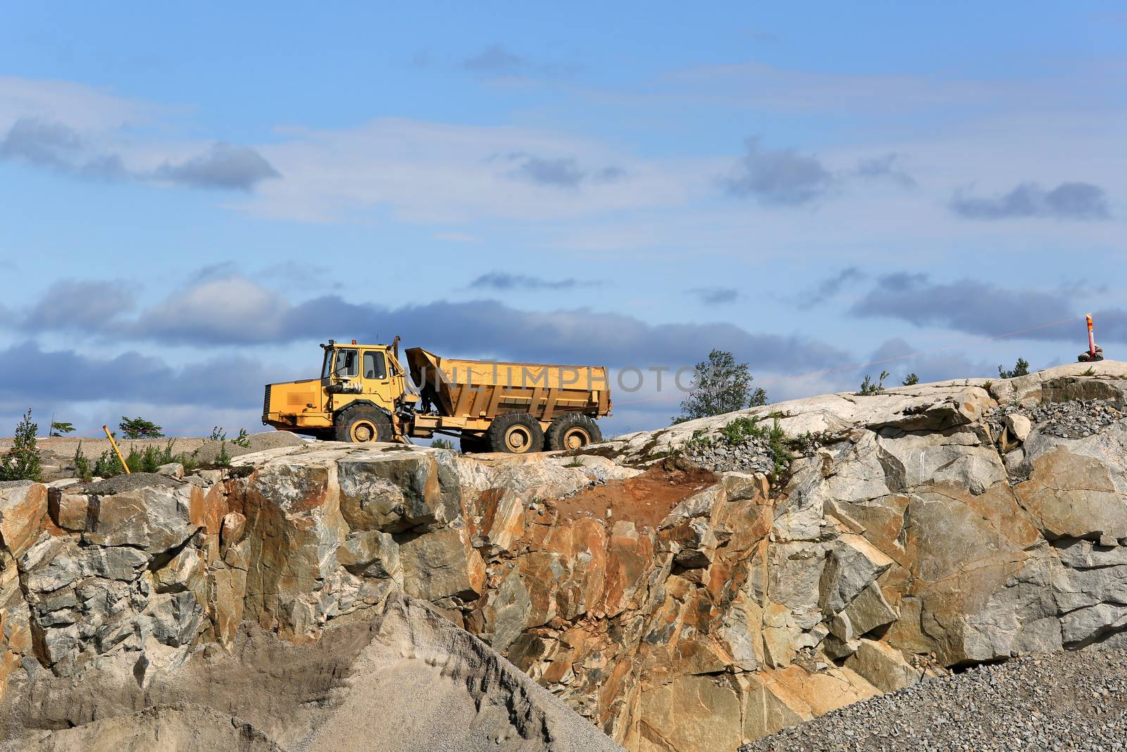 Landscape of a stone quarry with an articulated hauler and blue sky with some clouds.