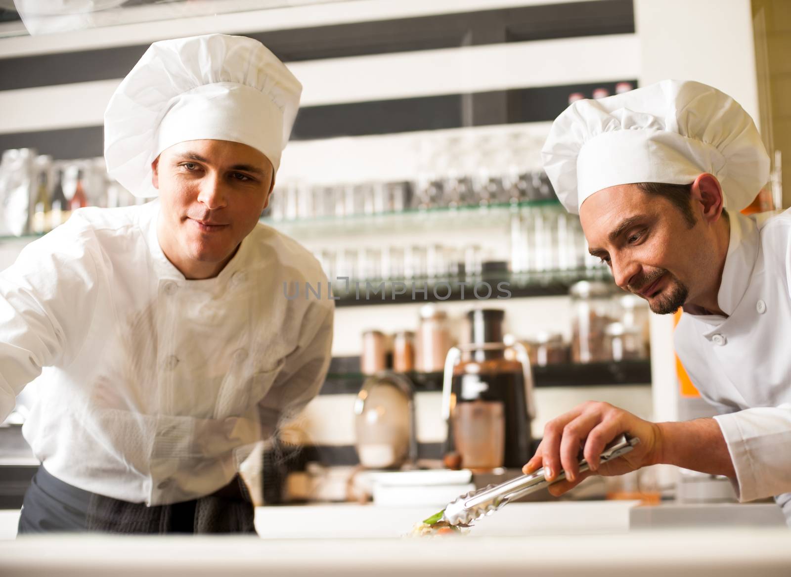 Chef watching his assistant arranging dish by stockyimages