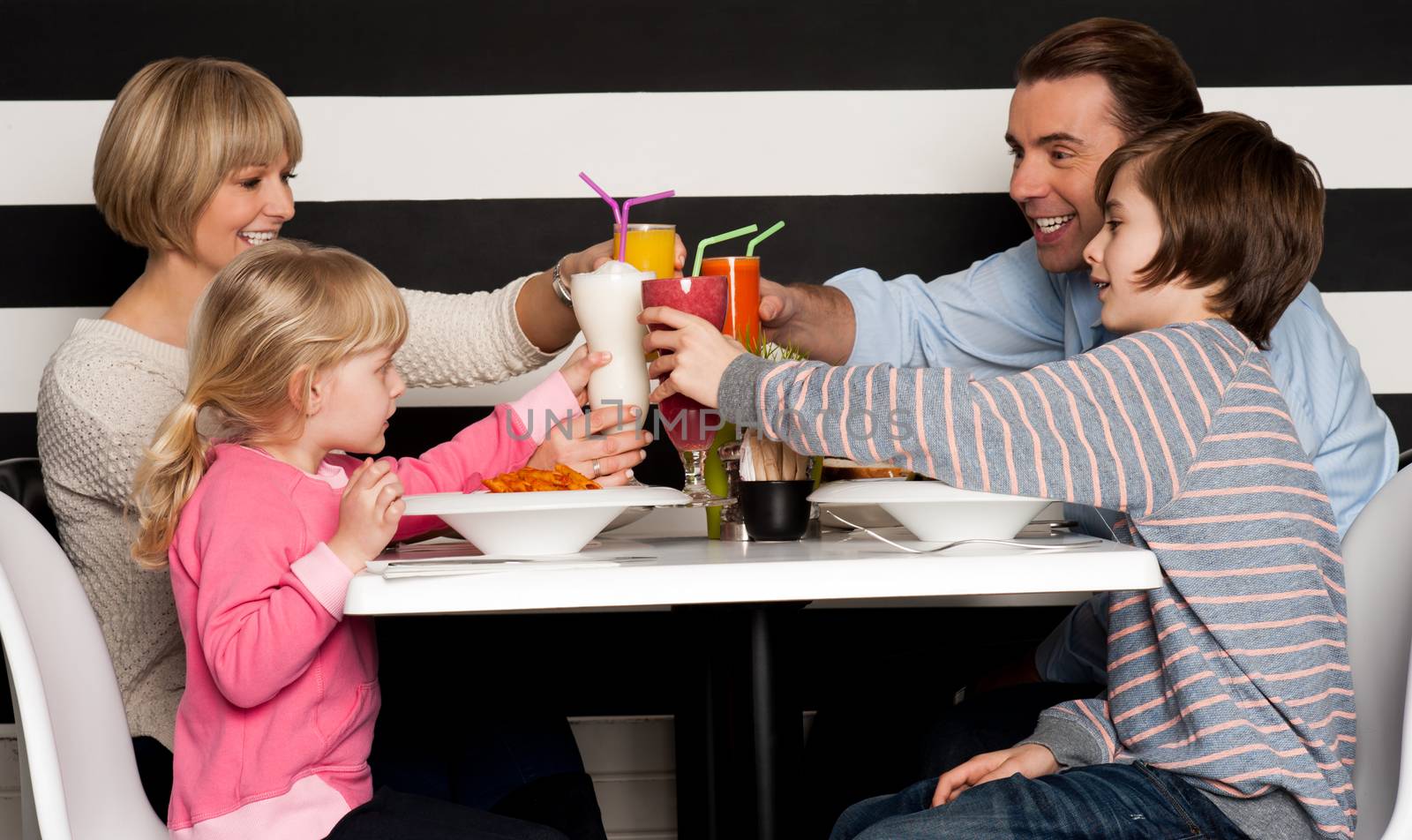 Family toasting smoothies in restaurant by stockyimages