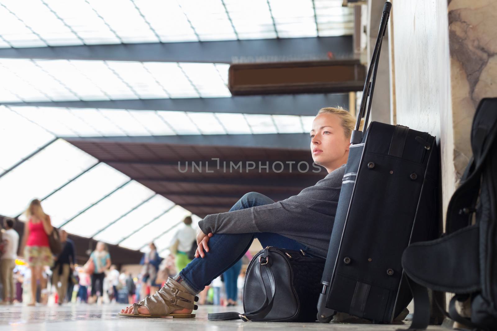 Tired female traveler waiting for departure, sitting on the station floor with all her luggage.