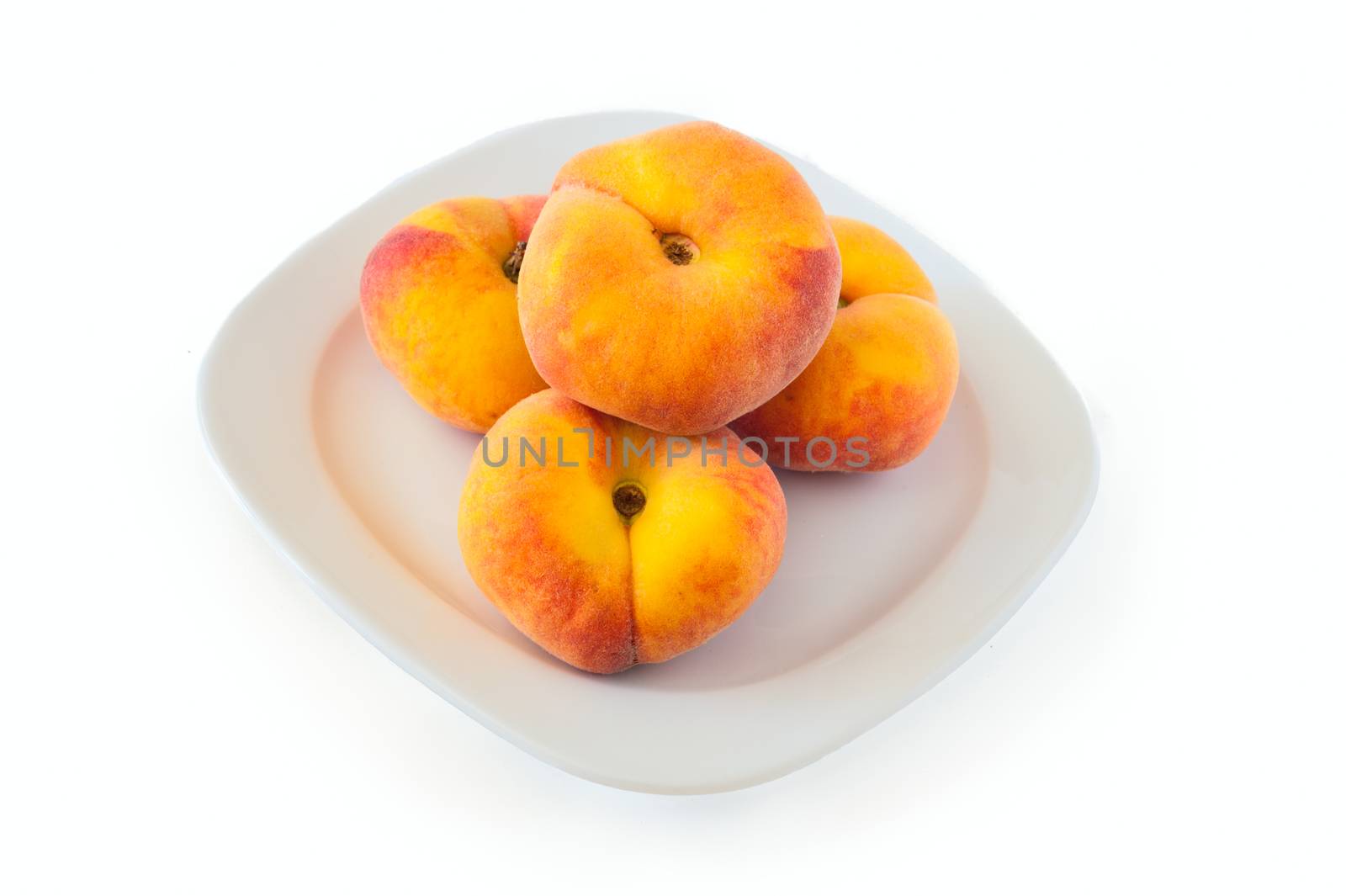 New variety of flat peaches lies on a white plate against a white background