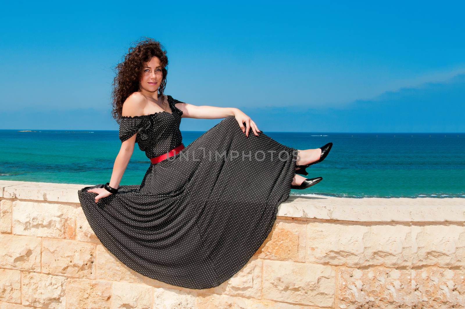 
Girl sitting on the parapet in a beautiful long dress and looks at the sea