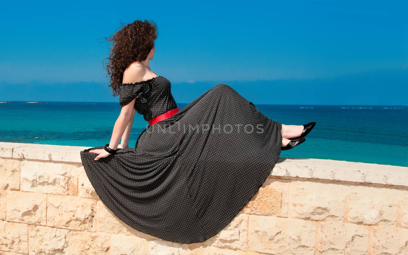 Girl sitting on the parapet in a beautiful long dress and posing for a photograph