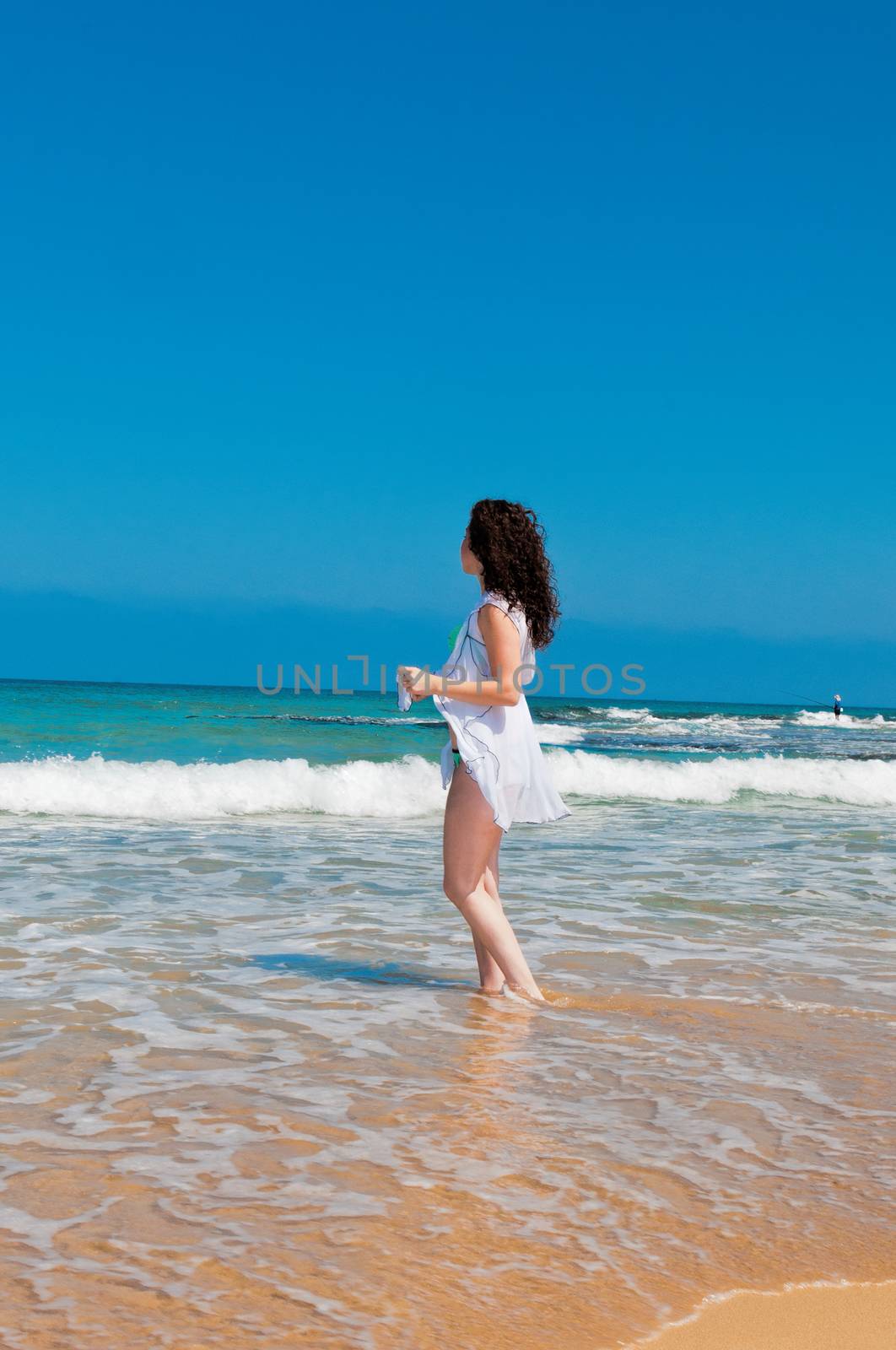 Girl in green bathing suit and white robe standing in the sea and looks into the distance