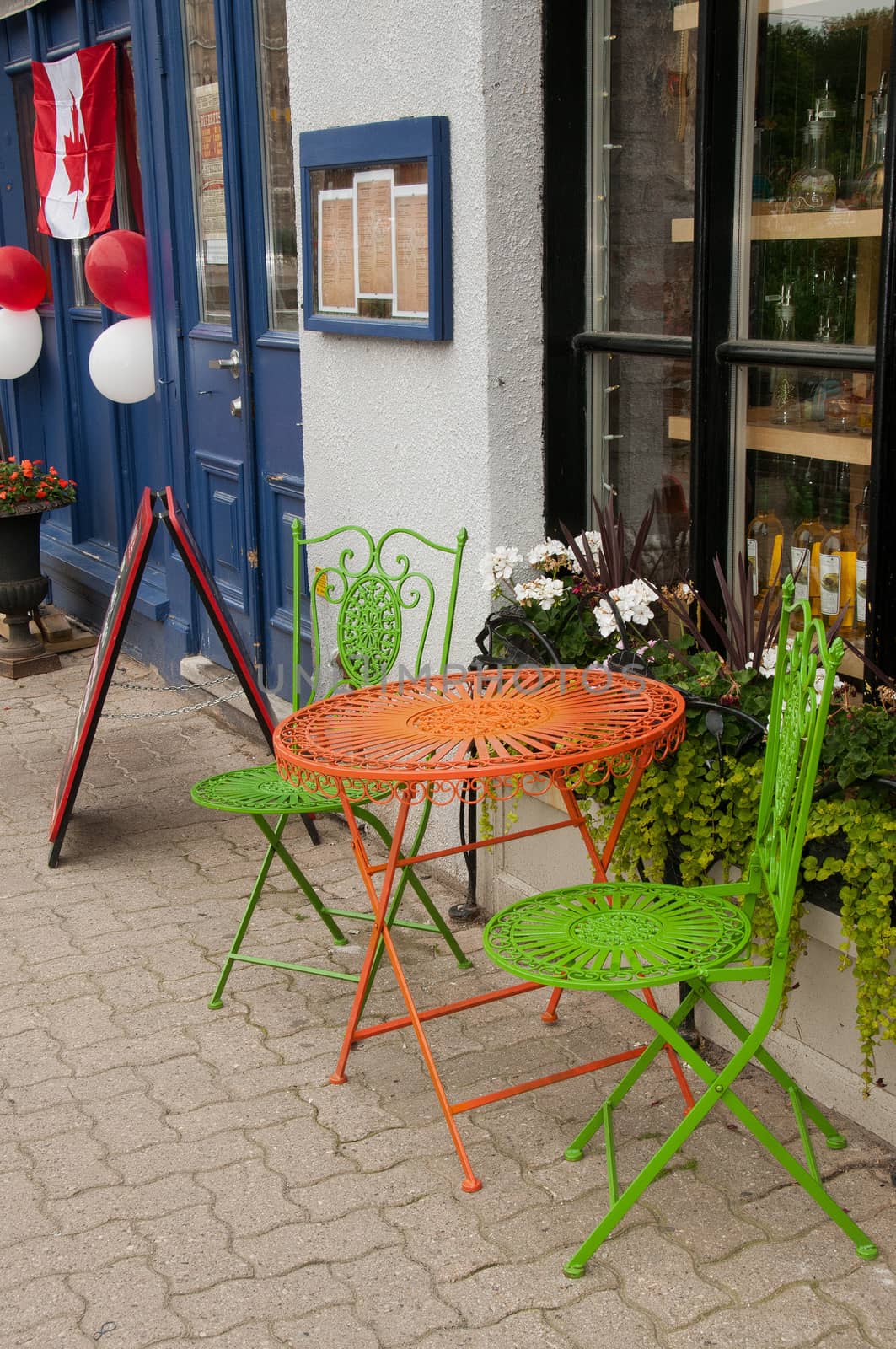 Round red metal table and a pair green metal chairs stand on the sidewalk outside the cafe