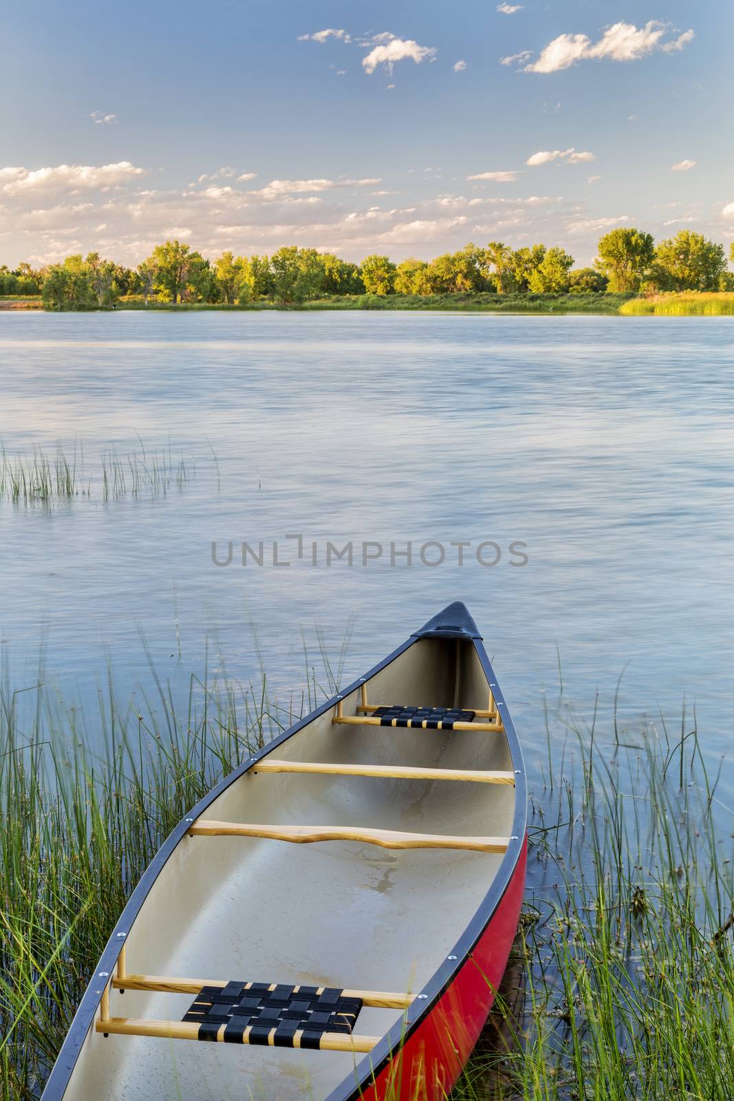 red canoe on a calm lake with a green grass - summer paddling concept