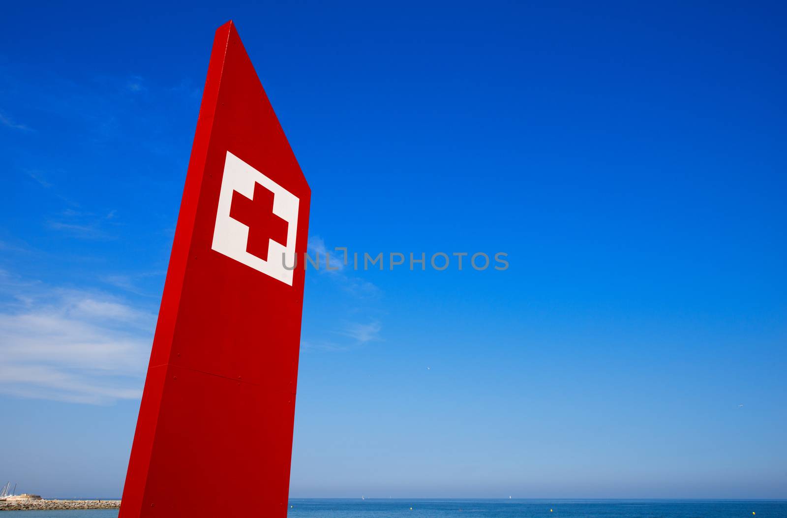 Red billboard with first aid symbol on blue sky and sea - Barceloneta beach in Barcelona, Spain