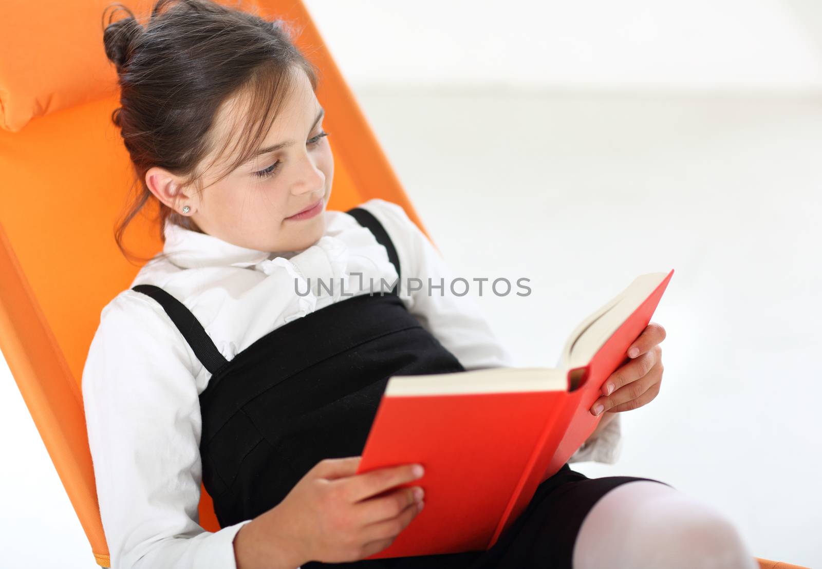 Joyful girl reading a book sitting on the orange chair