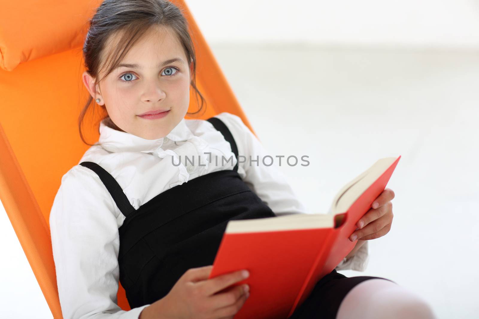 Joyful girl reading a book sitting on the orange chair