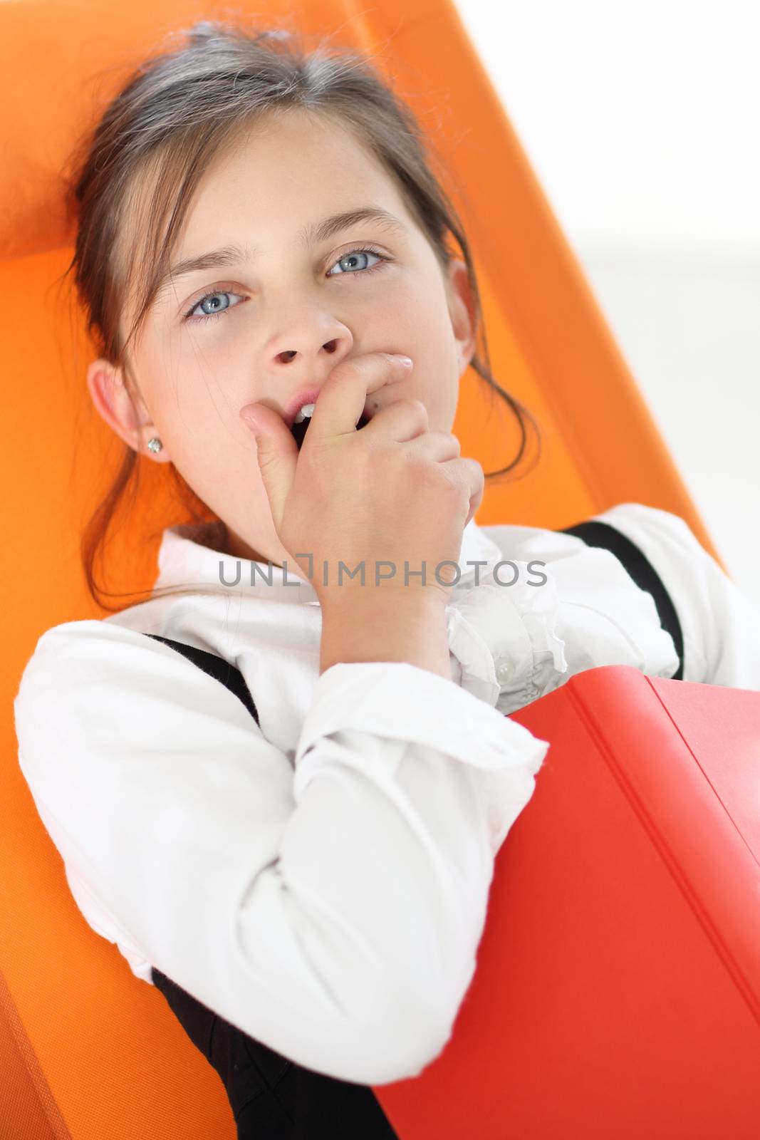 Joyful girl reading a book sitting on the orange chair