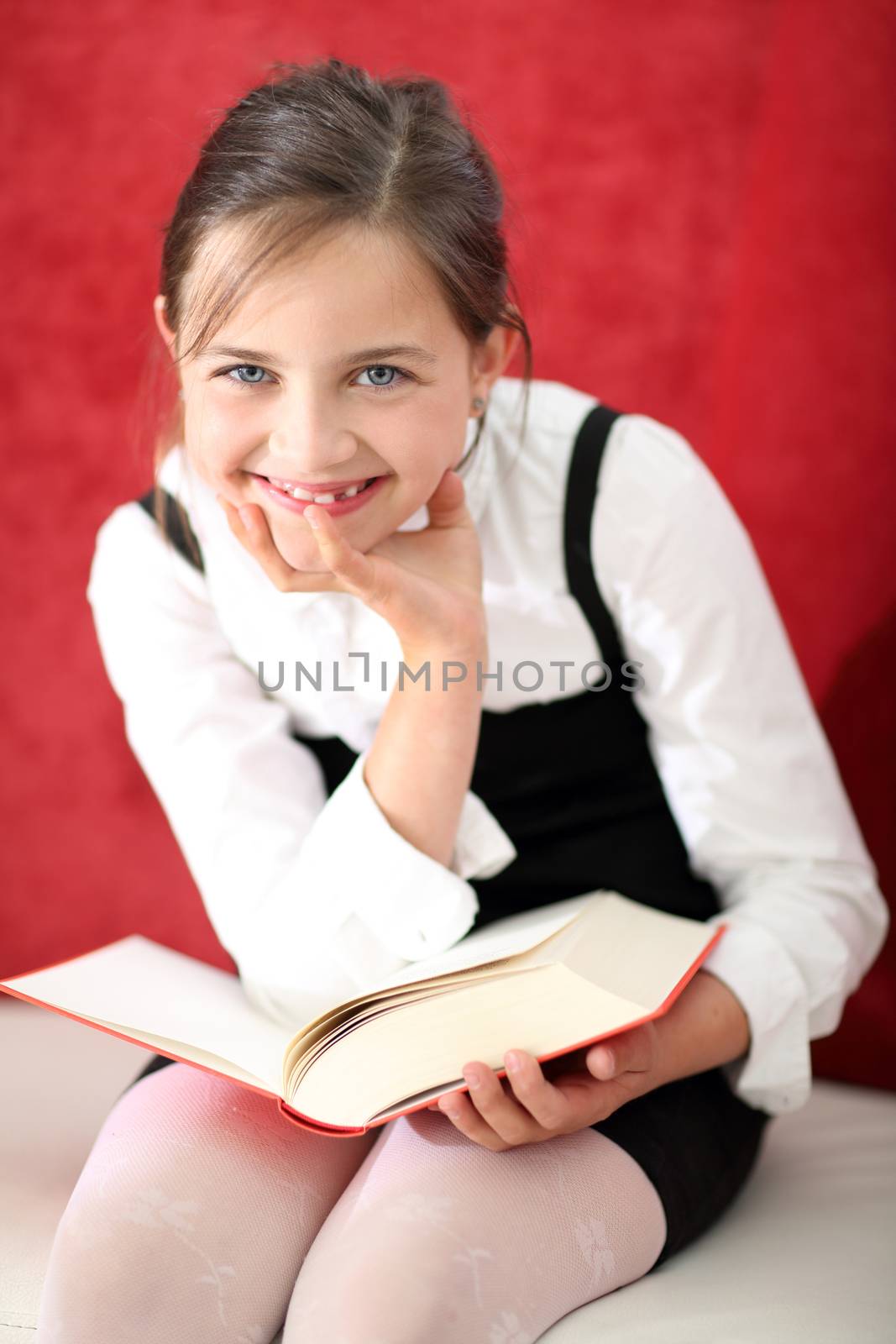 Joyful girl reading a book sitting on the orange chair