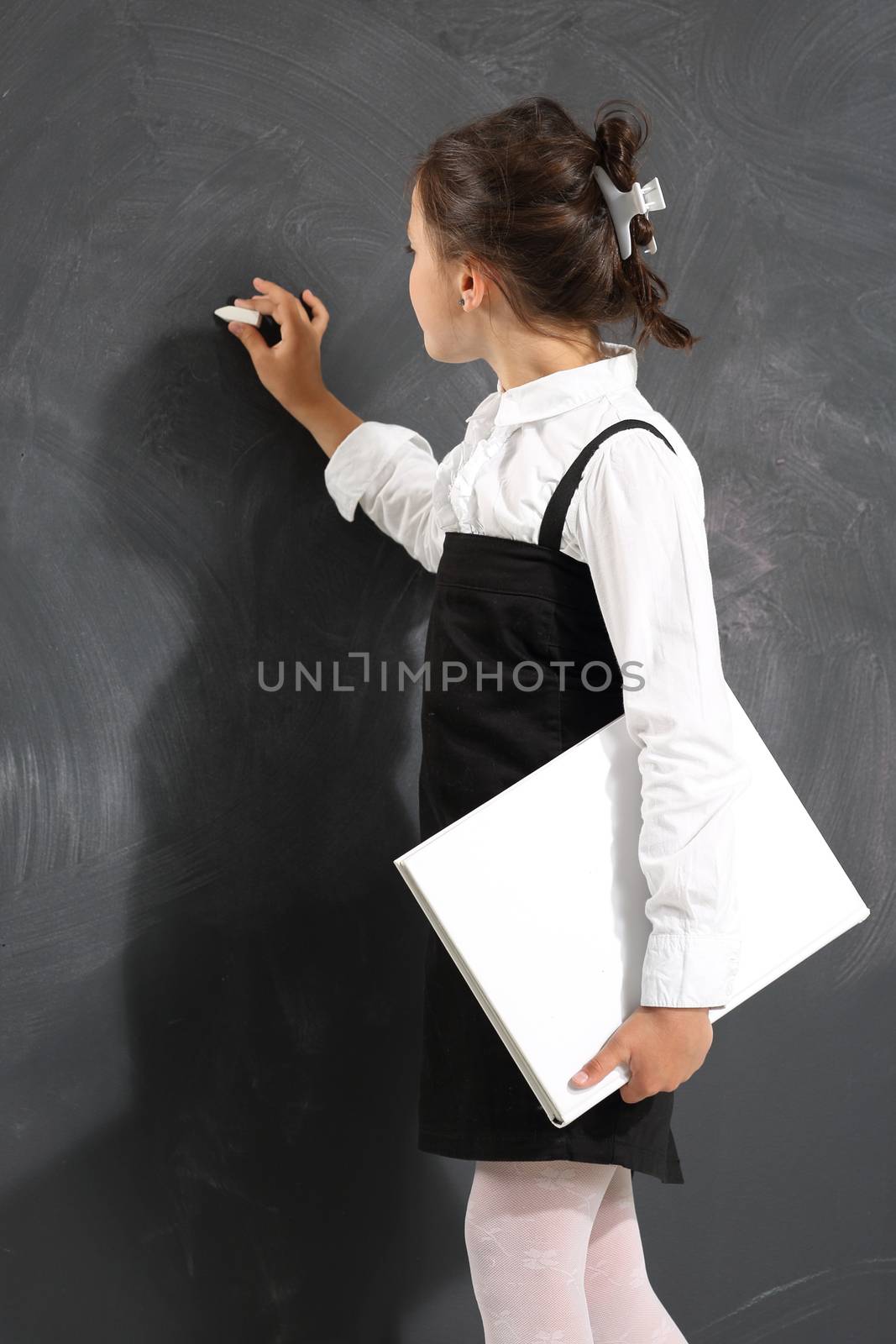 Schoolgirl holding heavy books standing on a background of black wall