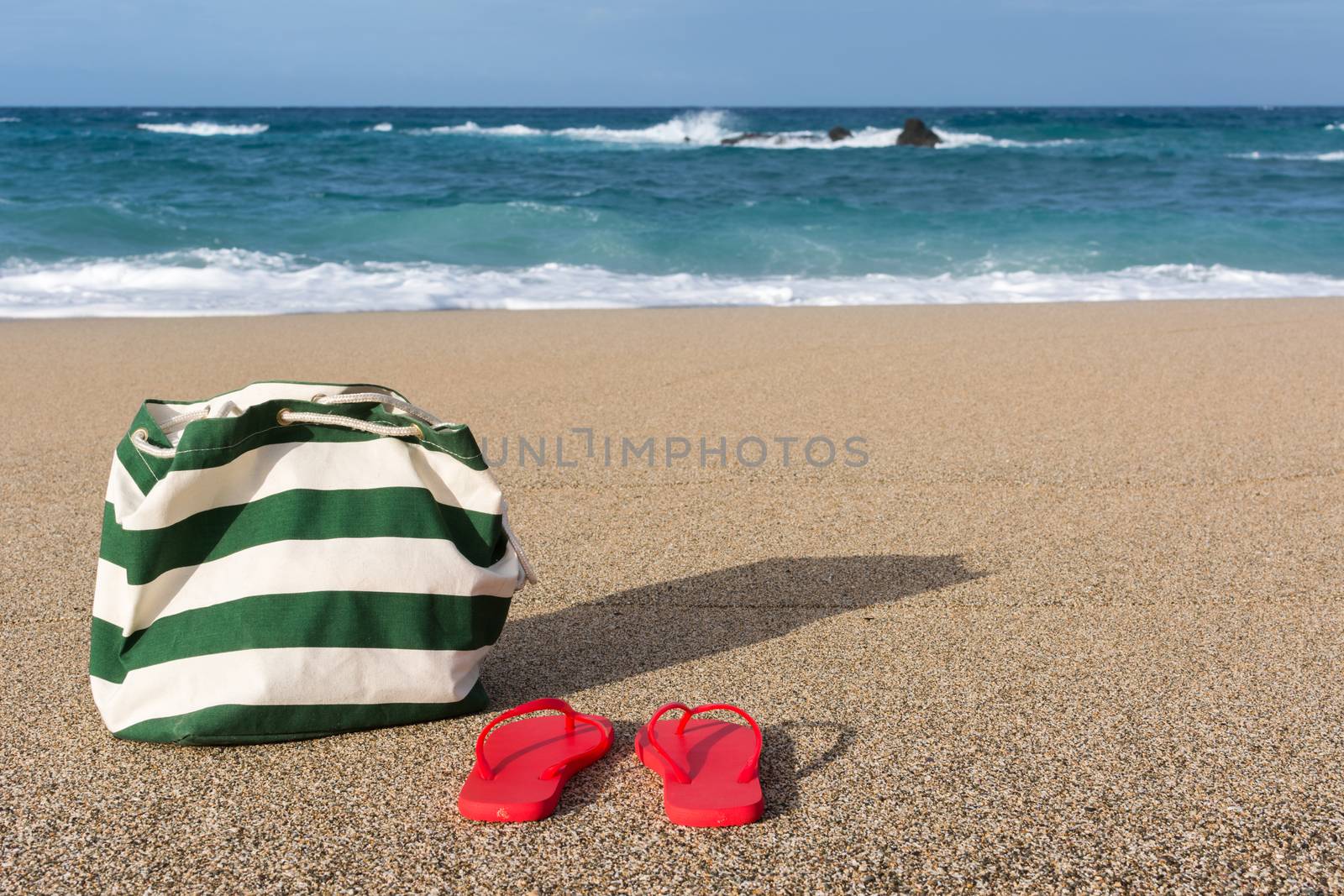 Summer concept of bag and flip flops on a tropical beach.