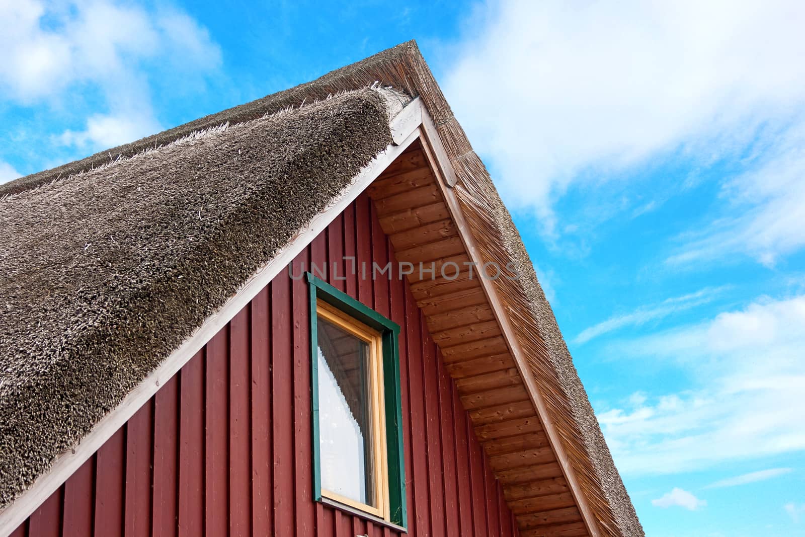roof of a thatched-roof house, blue cloudy sky in the background