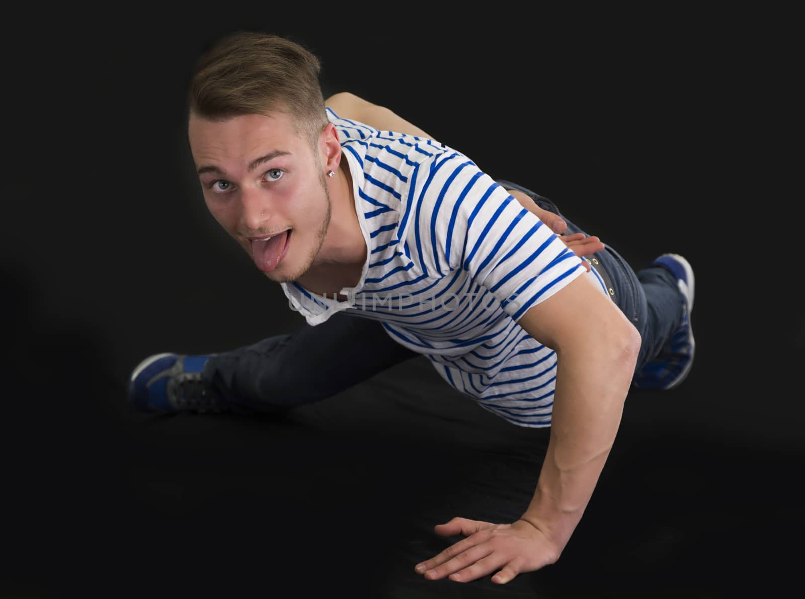 Handsome young man doing single hand push-ups, isolated on black background