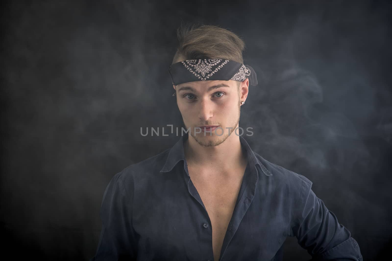 Handsome blond young man wearing bandana, smoke around him, dark background