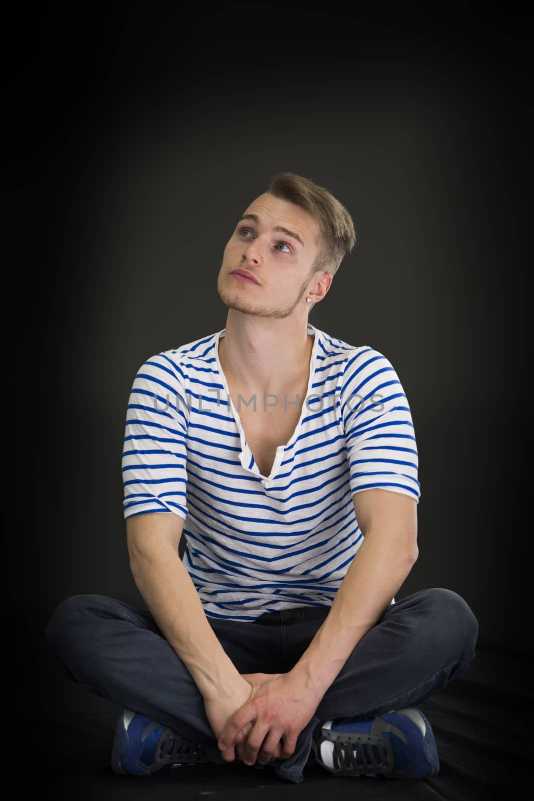 Handsome blond young man sitting on black background looking up thinking