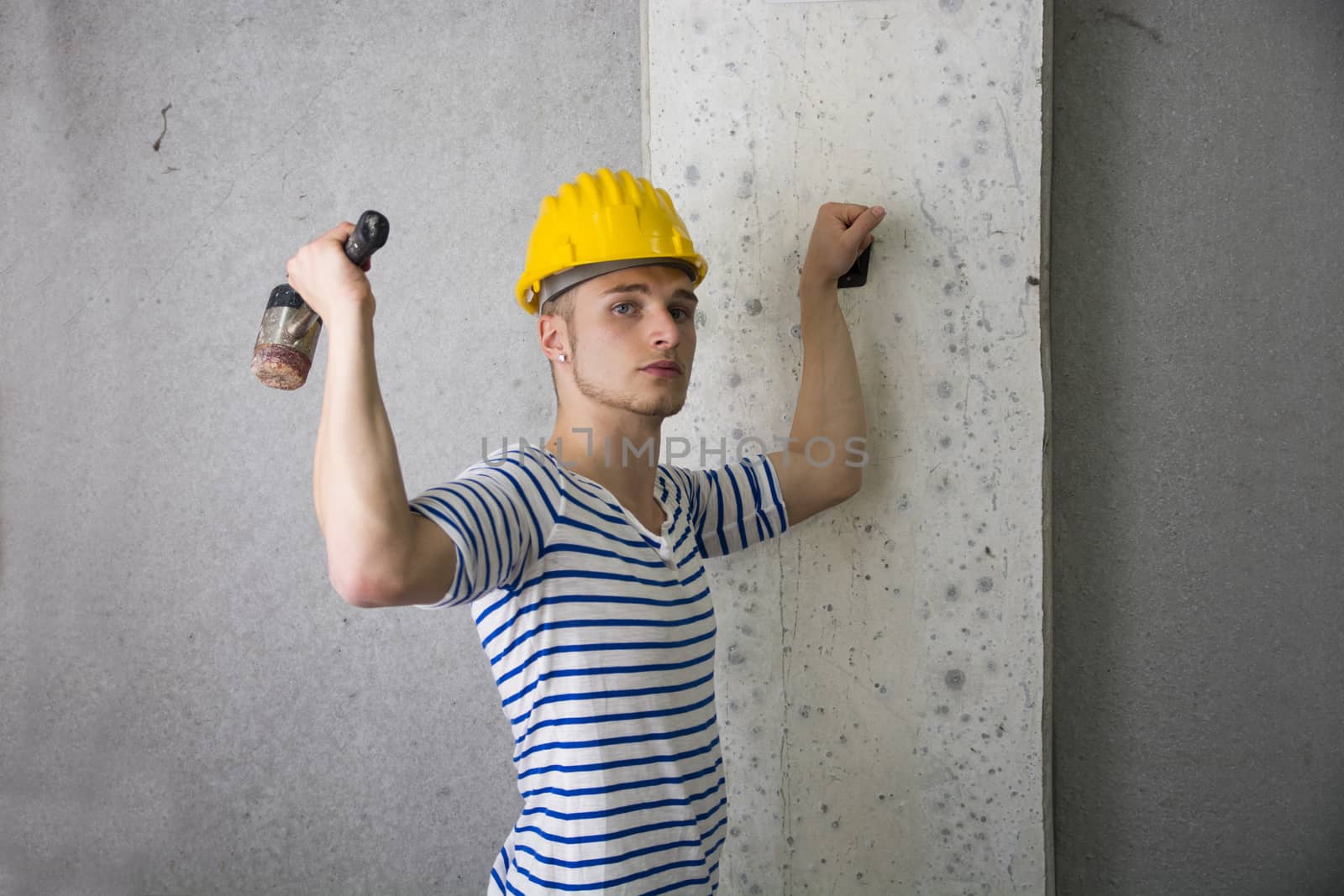 Handsome construction worker with yellow hard hat and hammer in hand