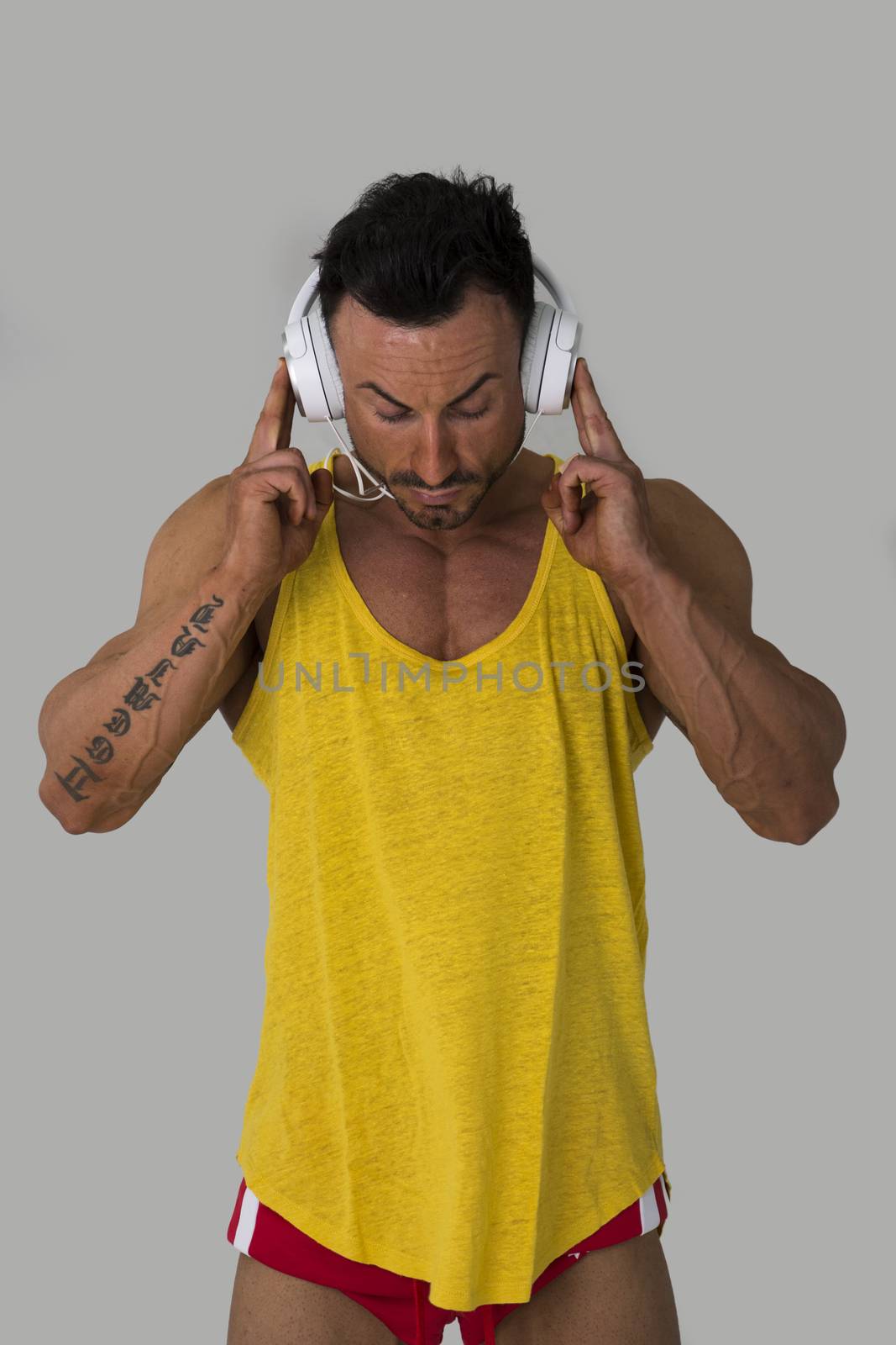 Muscular man standing, listening to music on headphones, looking down