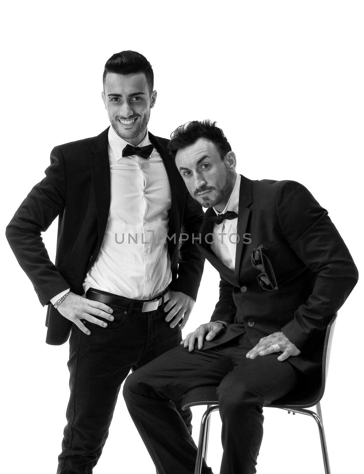 Two elegant men in suit and bowtie isolated on white, one standing, one sitting