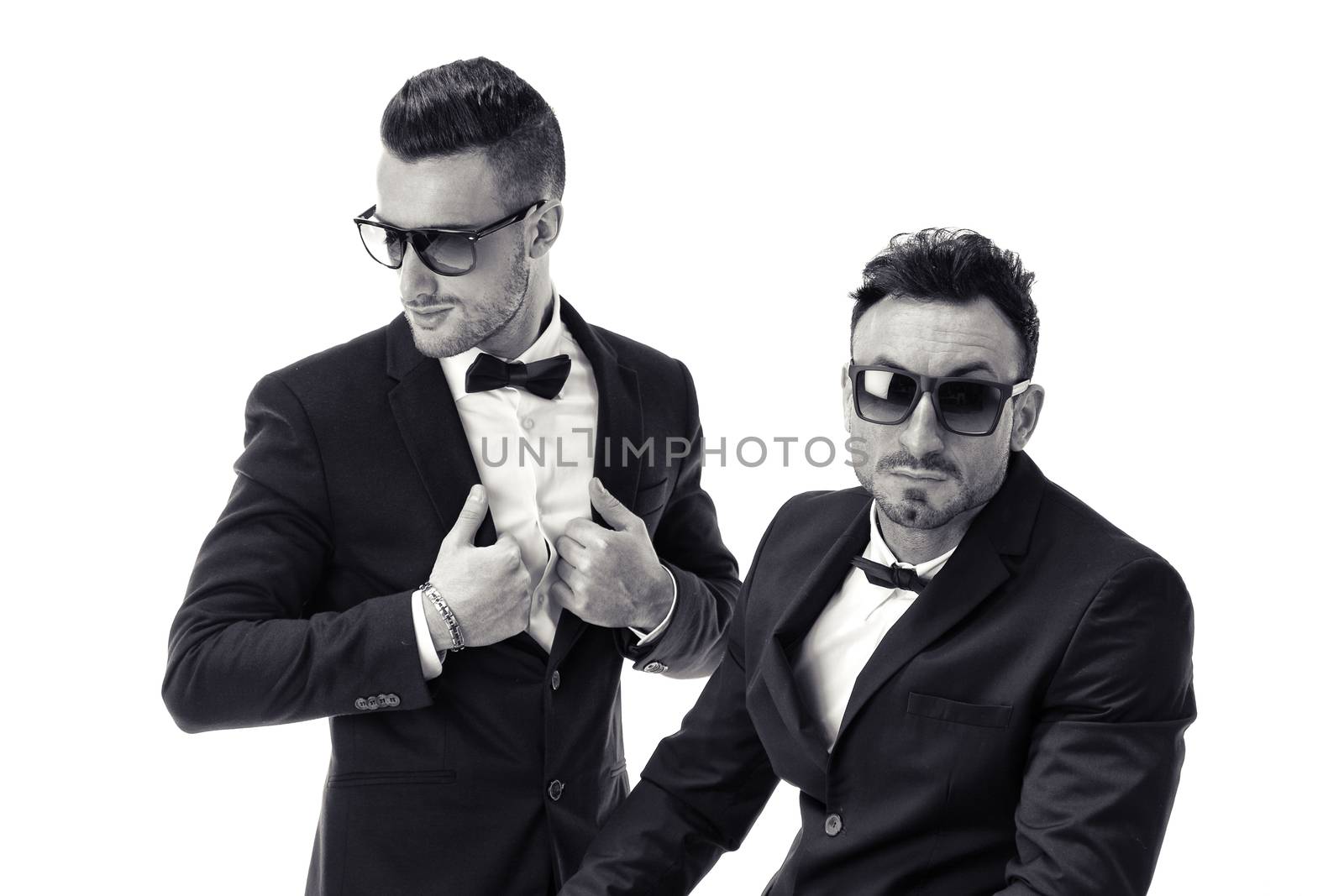 Two elegant men in suit and bowtie isolated on white, one standing, one sitting